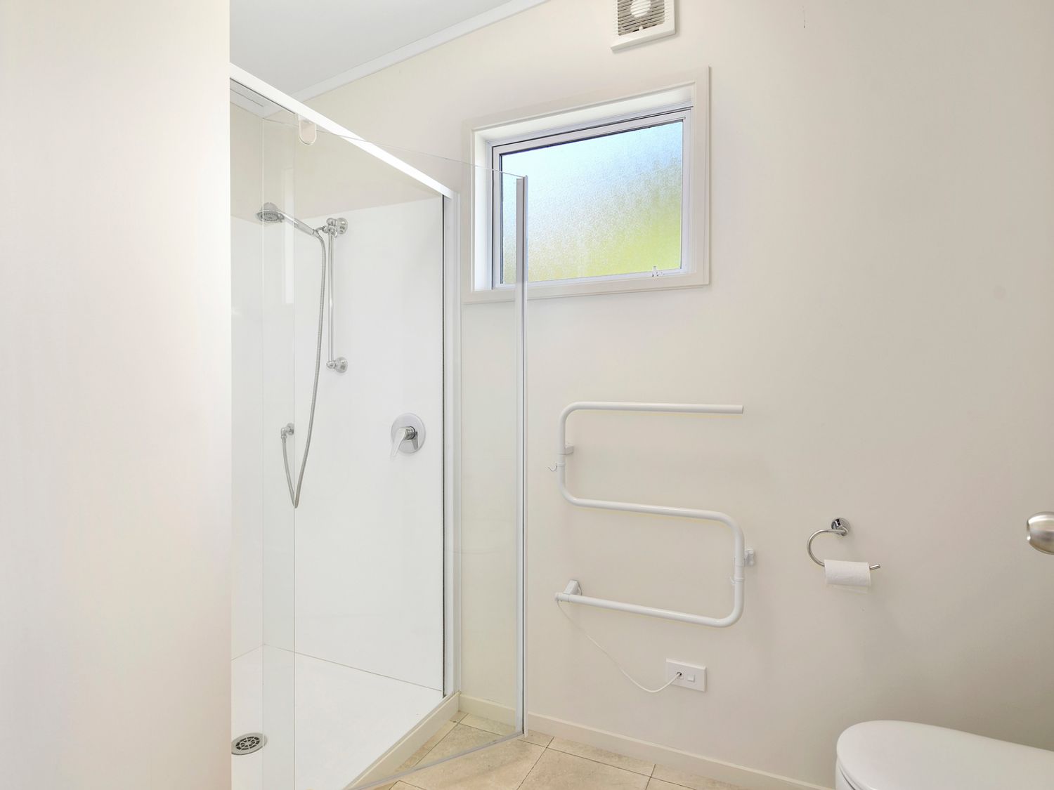 A bathroom with a glass shower enclosure a window a towel warmer a toilet paper holder and a toilet at Millard House - Marlborough Sounds