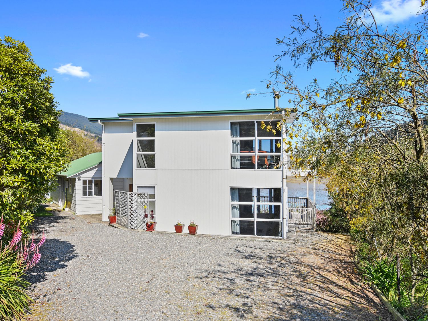 A two-story white house with large windows surrounded by trees and a gravel driveway at Millard House Marlborough Sounds