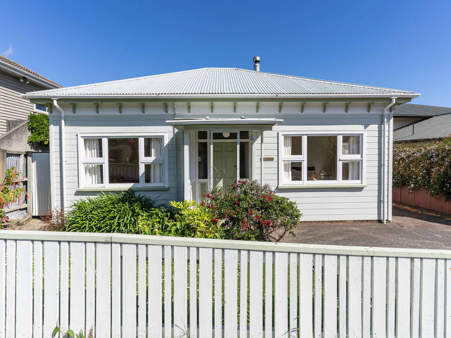 A single-story house with a white fence and garden in front at Le Solterre - Akaroa Holiday Home in Akaroa