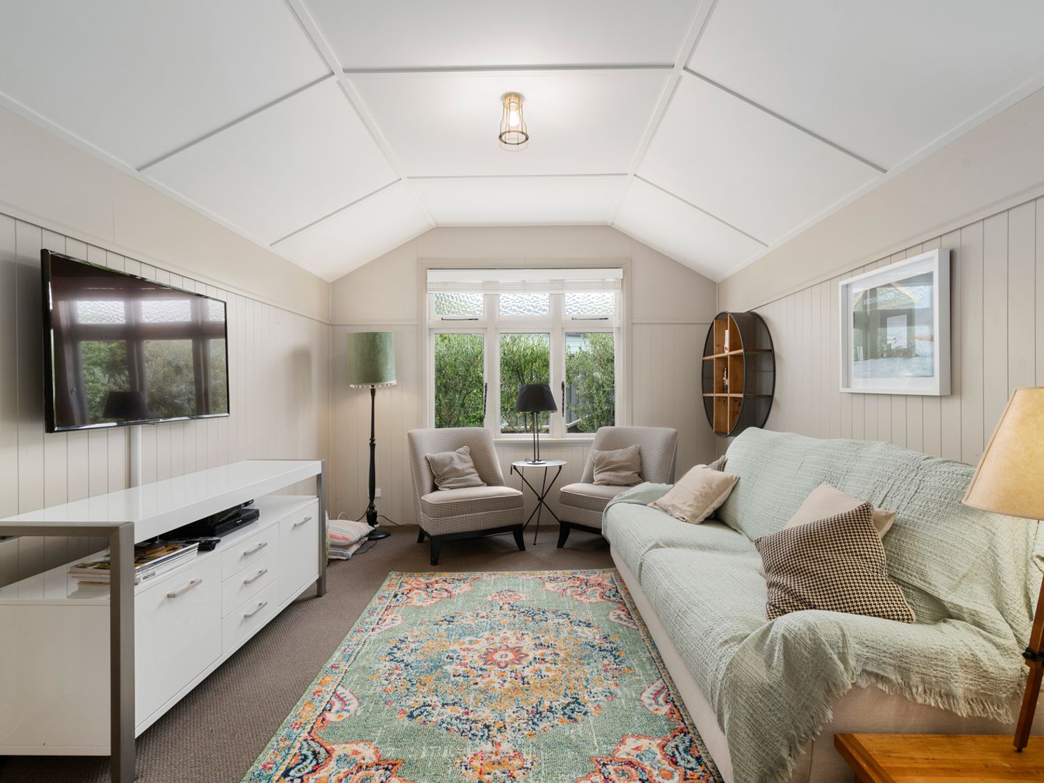 A living room with a sofa and two chairs around a small table a wall-mounted TV and a patterned rug at Cromwell Cutie Cromwell