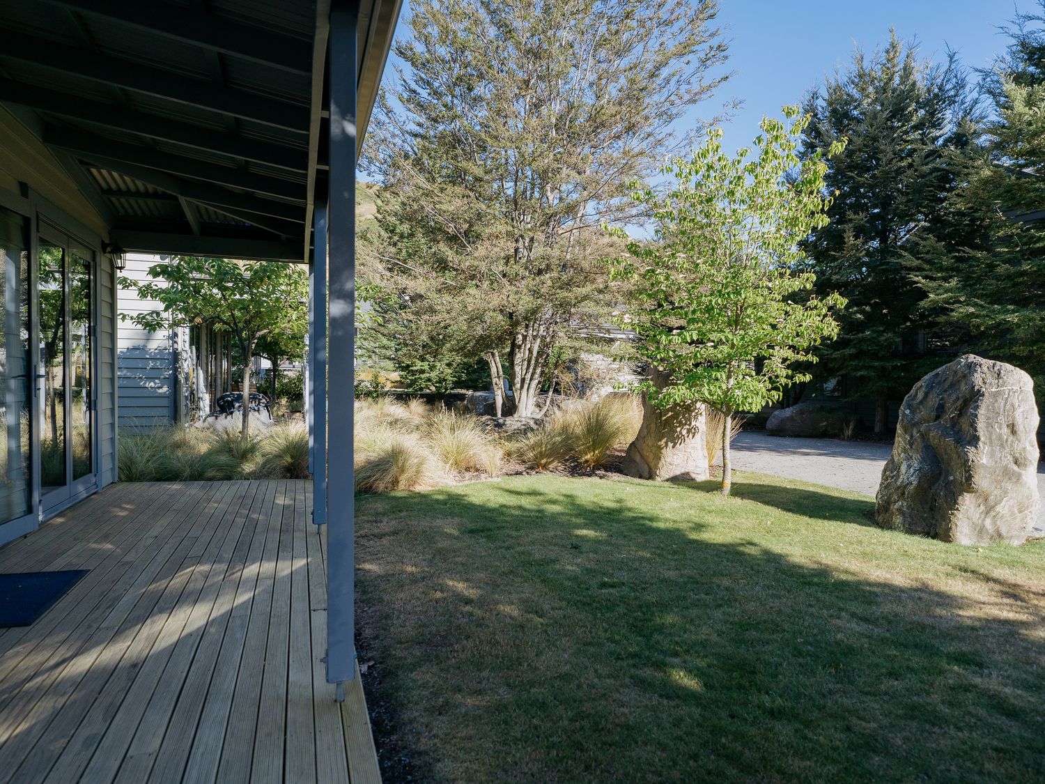 A garden view with trees large rocks and wooden deck at Cardrona Valley Escape - Cardrona Holiday Home in Cardrona