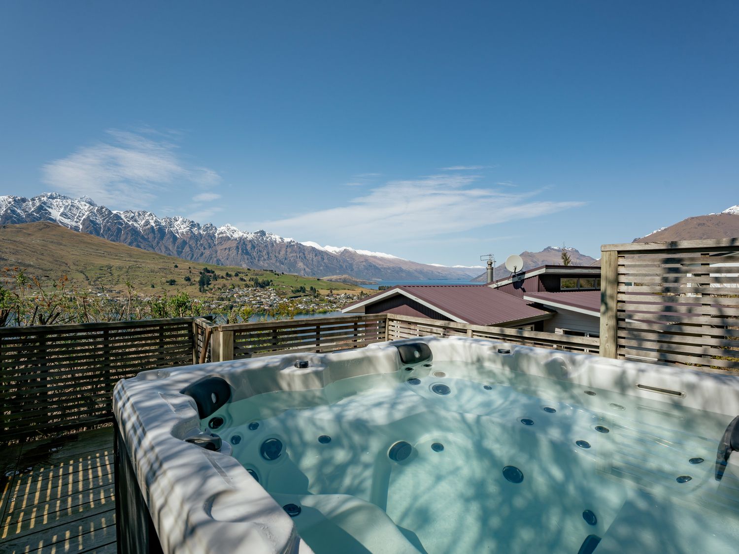 An outdoor hot tub on a wooden deck with slatted wooden fencing and snow-capped mountains in the background at Paradise Peaks Queenstown