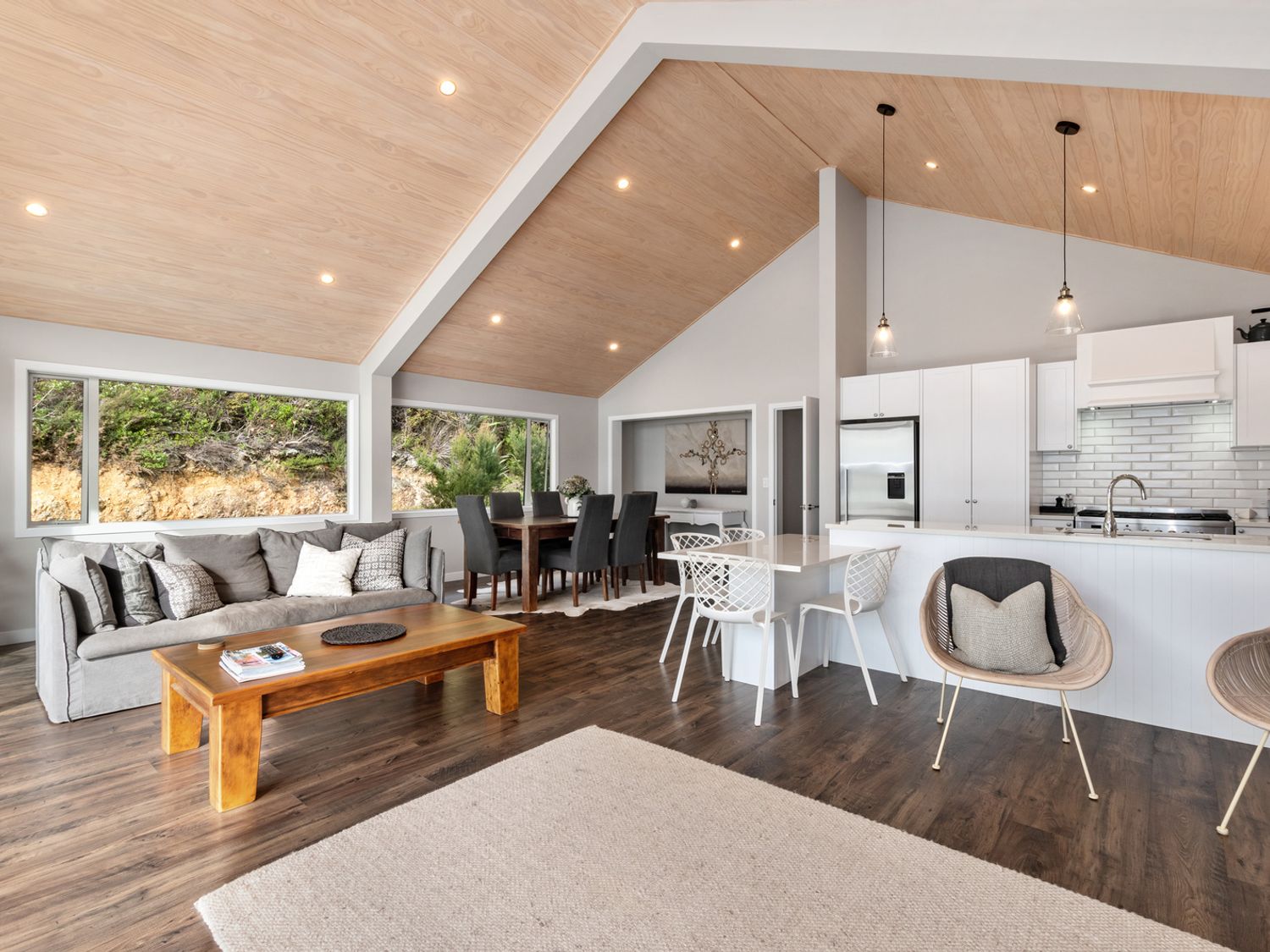 An open living space with a gray sofa and wooden coffee table dining area with dark chairs kitchen with white cabinets and island with chairs at Seaside Serenity - Kerikeri Holiday Home in Kerikeri