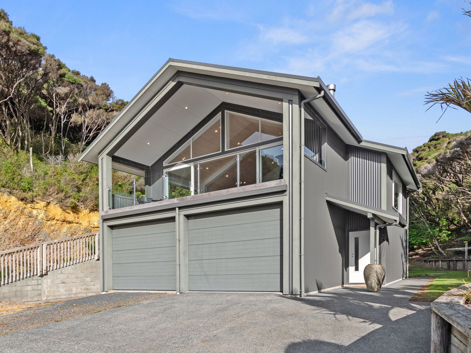 A two-story gray house with a double garage and a balcony surrounded by trees at Seaside Serenity - Kerikeri Holiday Home in Kerikeri