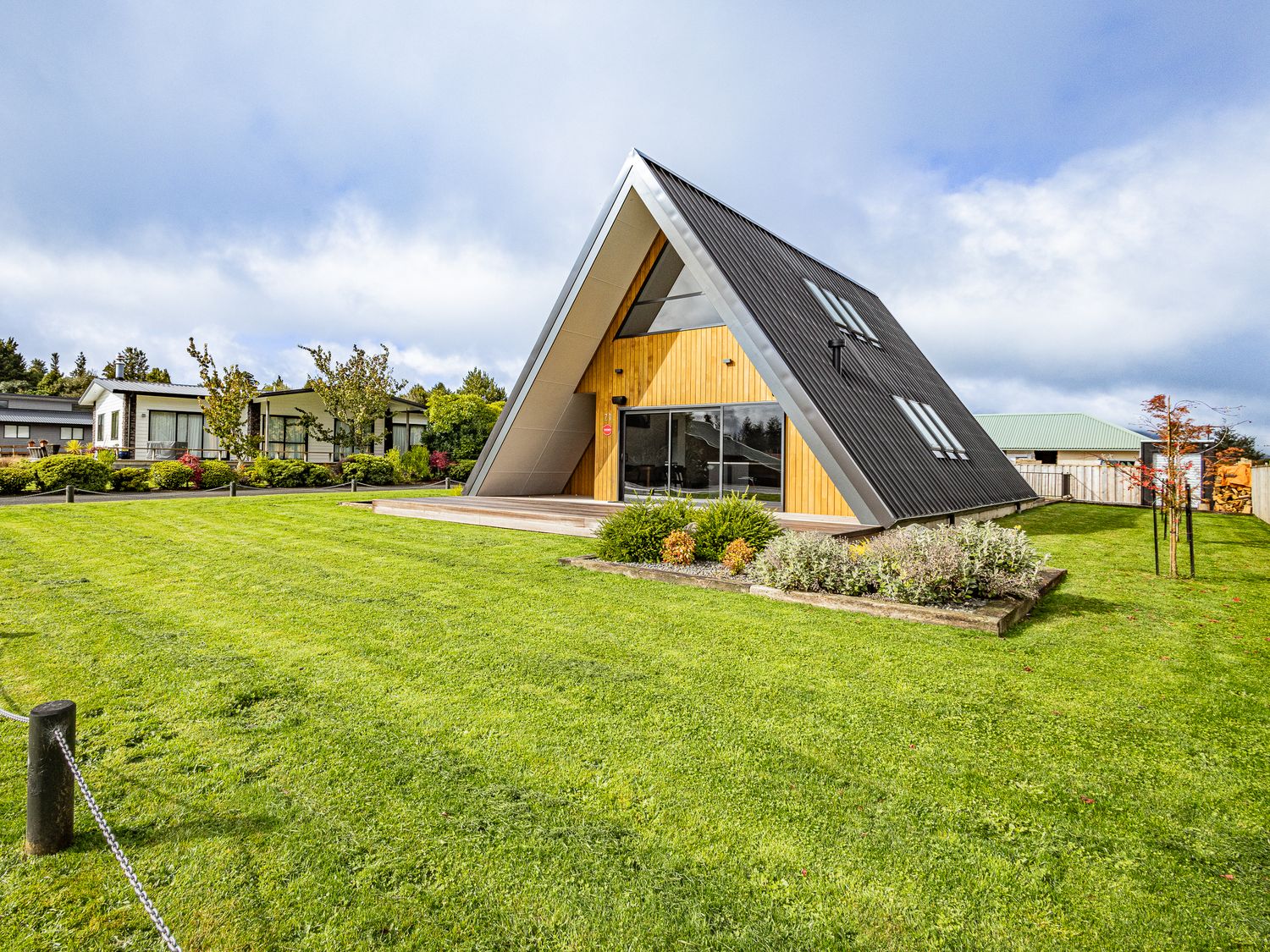 An A-frame house with a wooden deck and garden in a green lawn at Findlay Chalet - National Park Holiday Home in National Park
