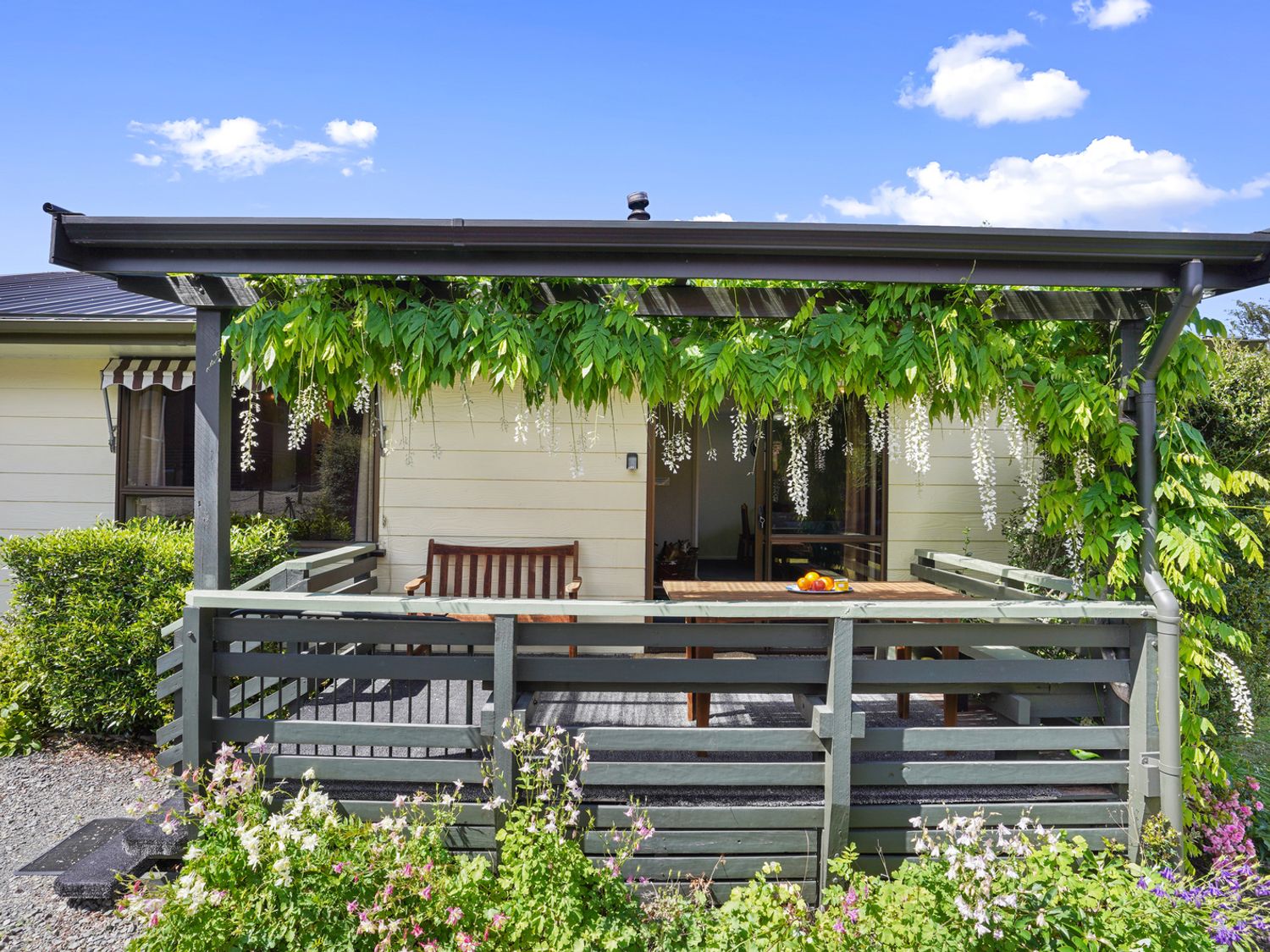A porch with wooden railing and furniture with flowering vines hanging at Hanmer Honey - Hanmer Springs Holiday Home in Hanmer Springs