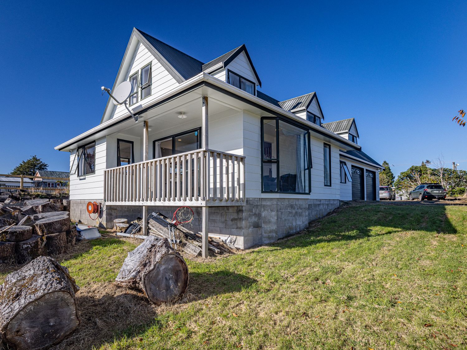 An exterior view of a two-story house with a porch a satellite dish and parked cars on a grassy lawn at Three Peak Lodge - National Park Holiday Home in National Park