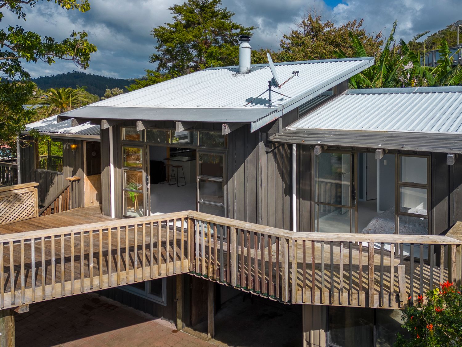 Exterior view of a wooden house with a metal roof and wooden deck surrounded by trees at Paku View Retreat - Tairua Holiday Home in Tairua