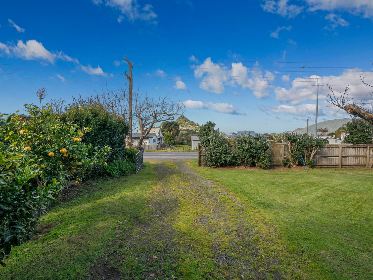 A backyard with a grassy path leading to a road with houses and hills in the background at Paku View Retreat Tairua Holiday Home in Tairua