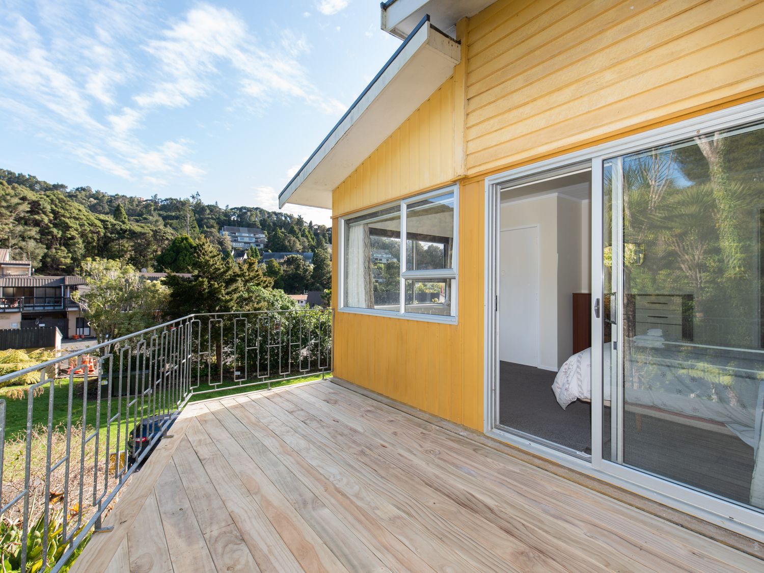 A wooden deck balcony with metal railing outside a yellow house in a residential area at Knight's Retreat - Paihia Holiday Home Paihia