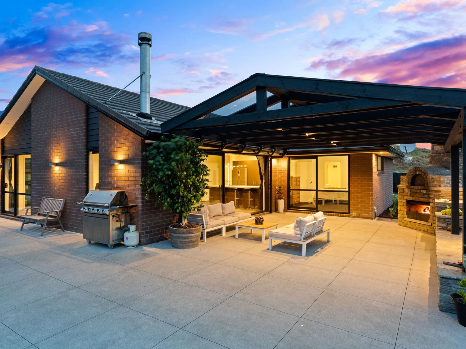 An outdoor patio area with seating, a grill, a wood-fired oven, and a covered roof at Mangawhai Maketu in Mangawhai