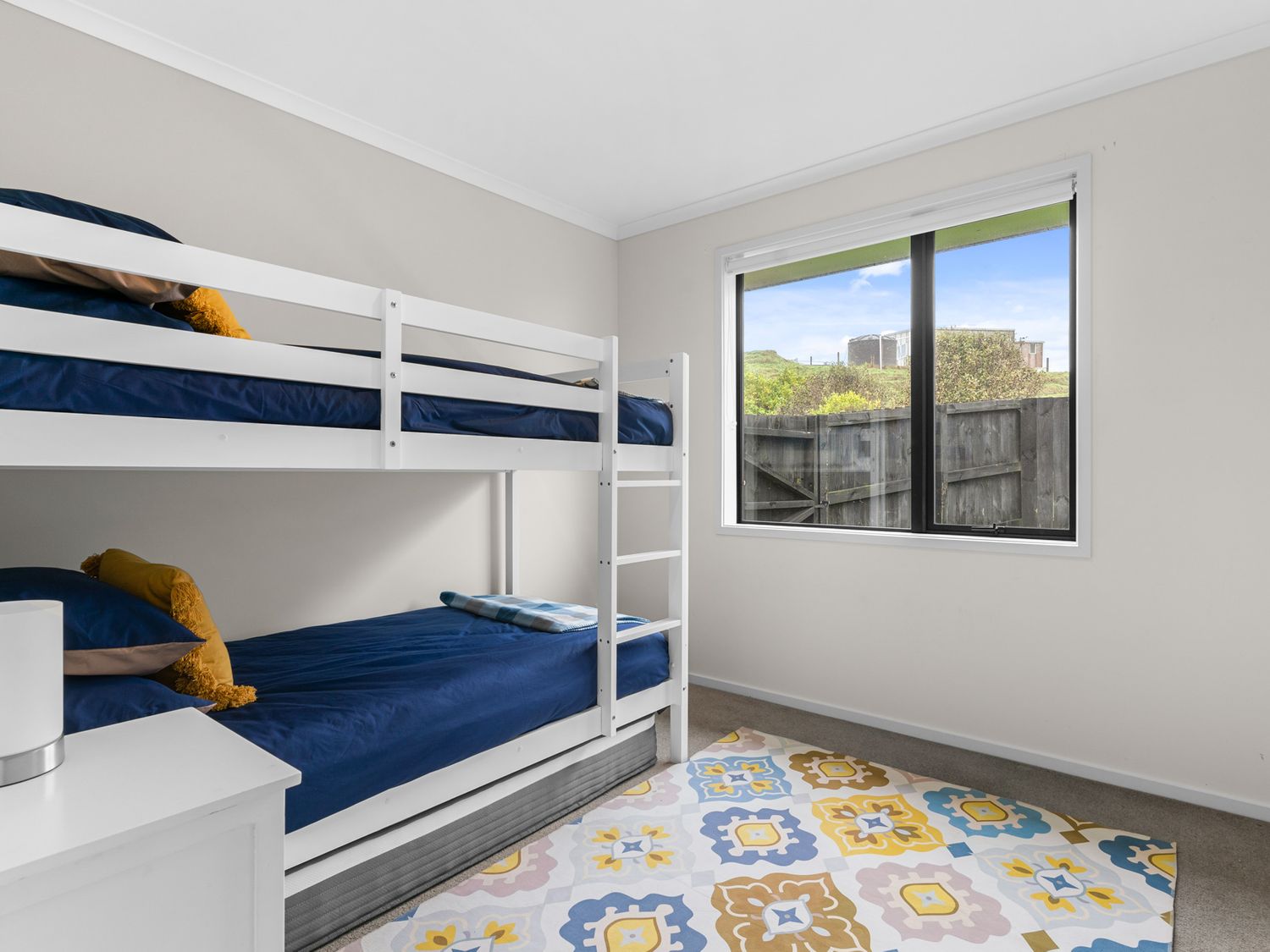 A bedroom with white bunk beds and a patterned rug near a window at Mangawhai Maketu Mangawhai
