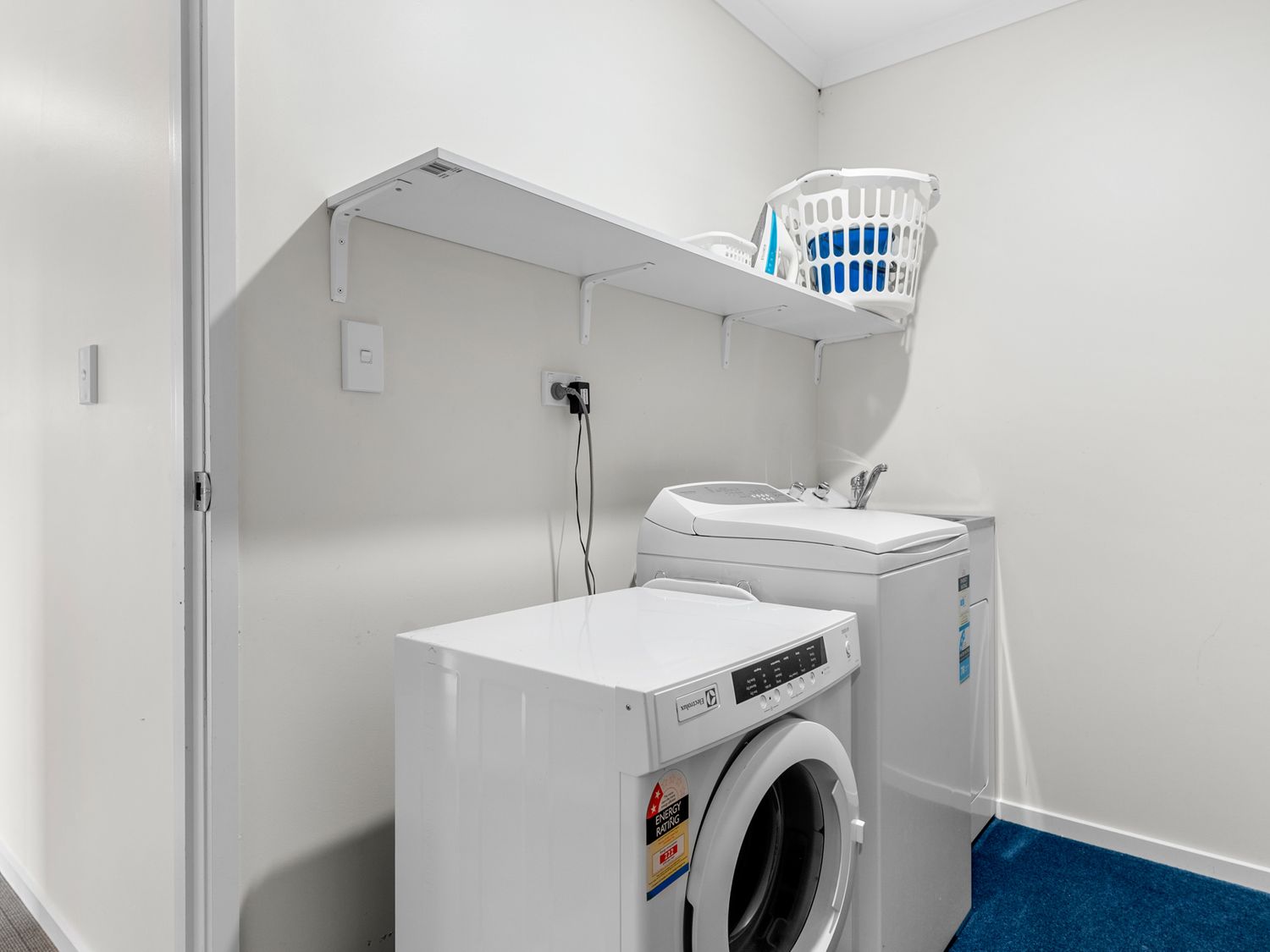 A laundry room with a front load washing machine top load washing machine a shelf and laundry baskets at Mangawhai Maketu Mangawhai Holiday Home Mangawhai