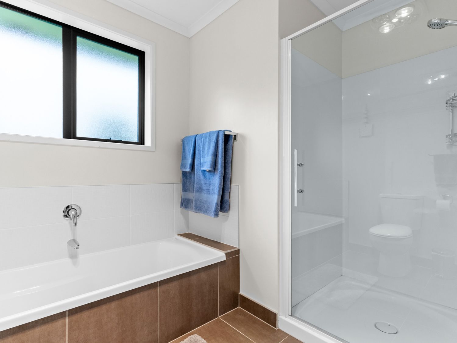 A bathroom with a bathtub, a glass-enclosed shower, a toilet, and blue towels hanging on a rack at Mangawhai Maketu Mangawhai Holiday Home