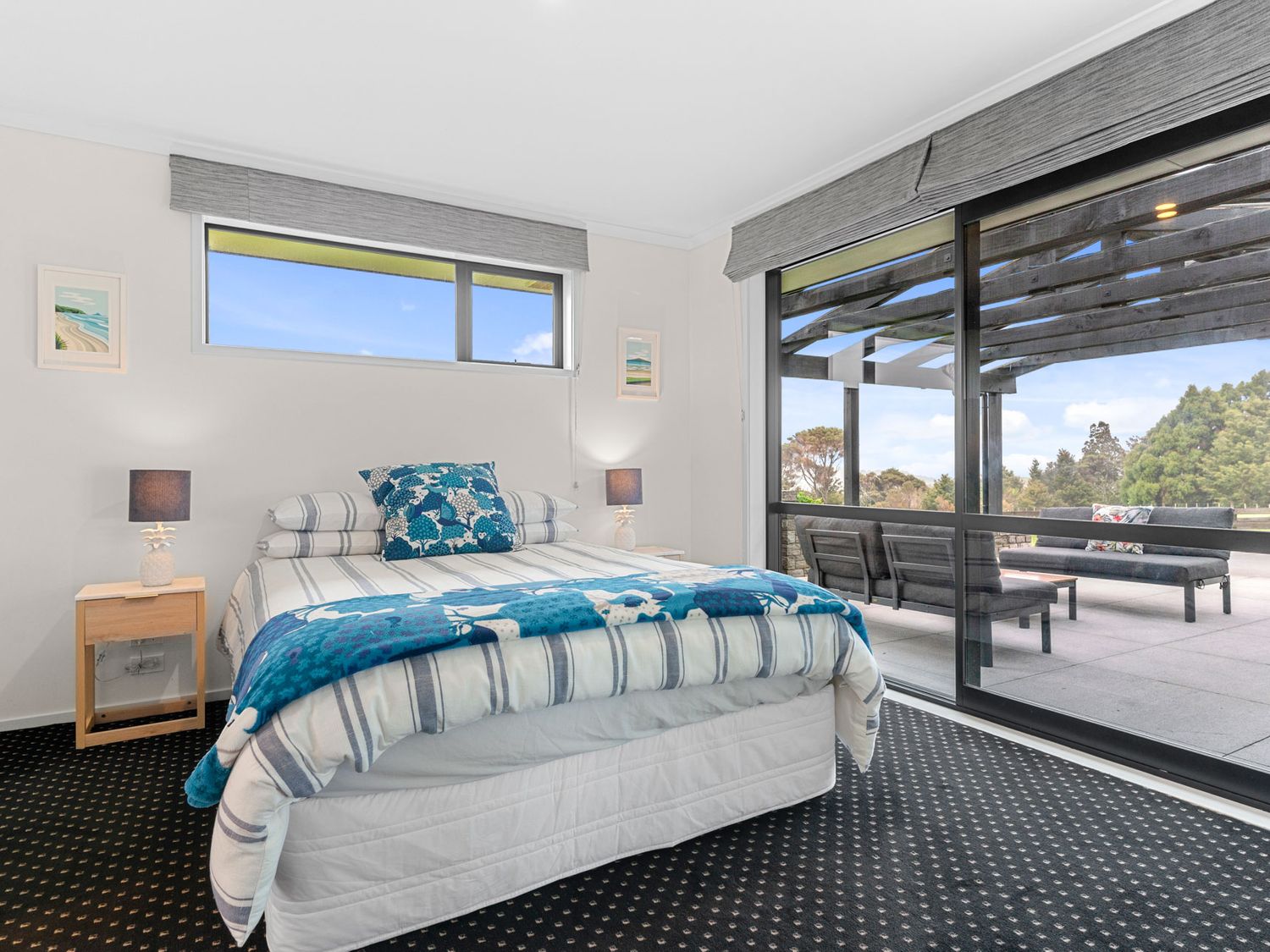 A bedroom with a bed bedside tables lamps and sliding glass doors leading to an outdoor seating area at Mangawhai Maketu - Mangawhai Holiday Home Mangawhai