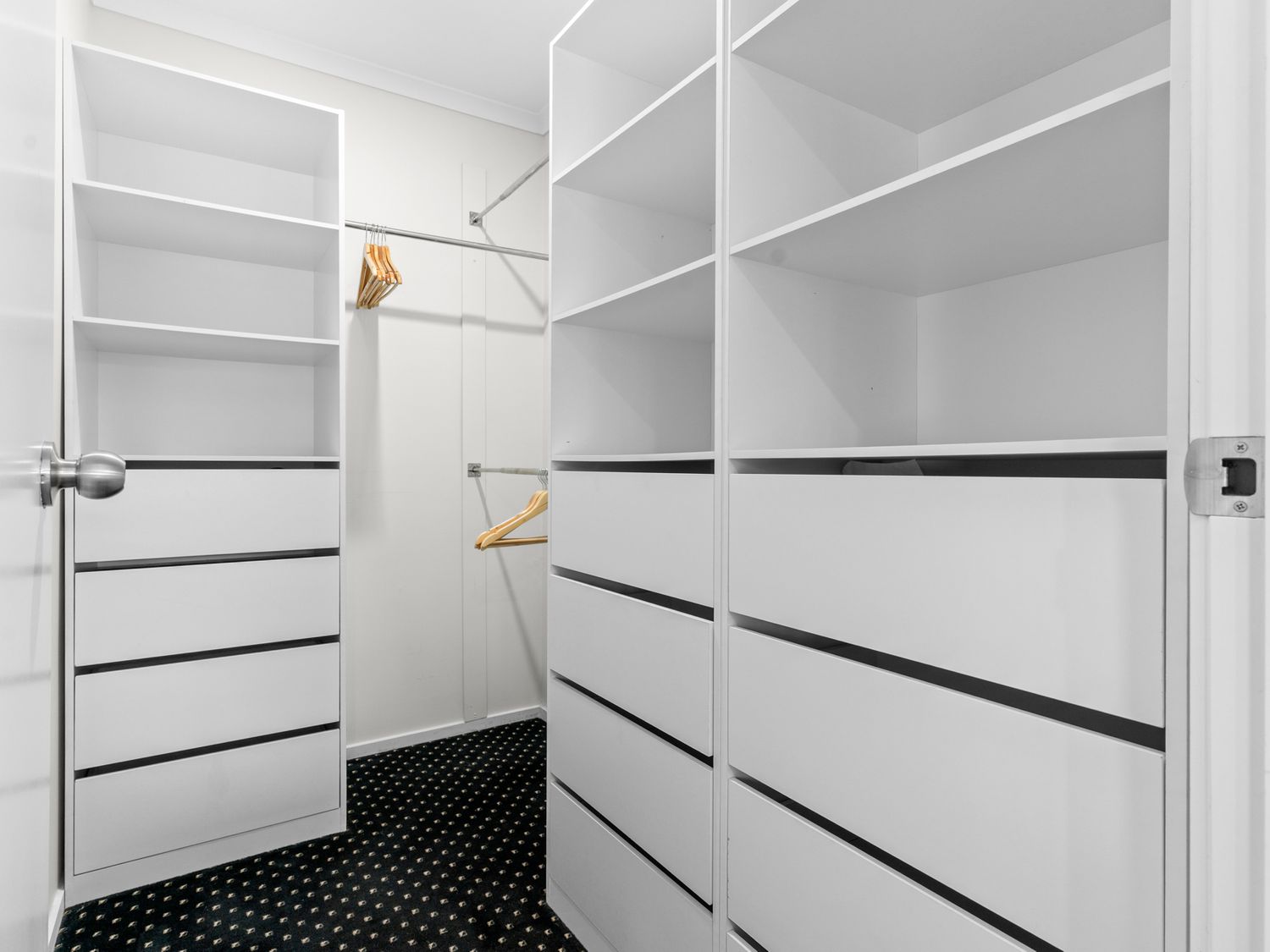 A walk-in closet with white shelves drawers and hanging rods with wooden hangers at Mangawhai Maketu Mangawhai Holiday Home