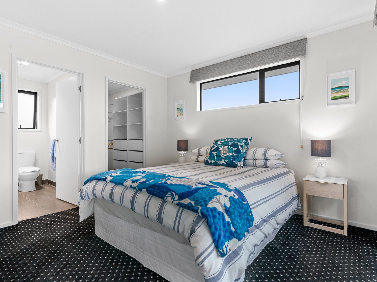 A bedroom with a bed with blue and white striped bedding a window above and a door leading to a bathroom and closet at Mangawhai Maketu Mangawhai