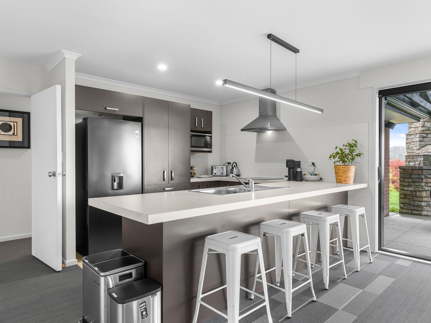 A kitchen with a large island countertop and four white bar stools at Mangawhai Maketu Mangawhai Holiday Home