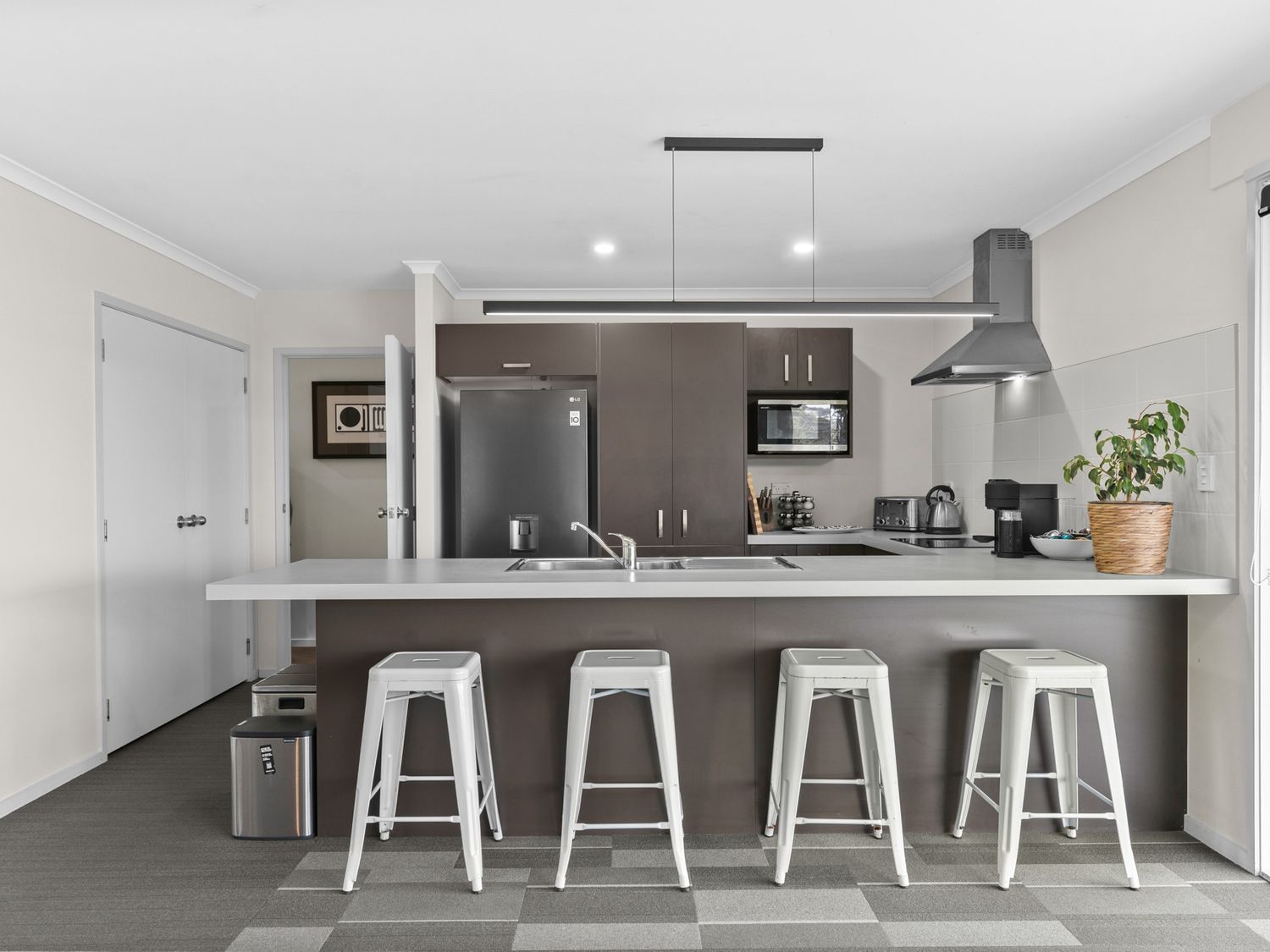 A modern kitchen with a large island and four white stools at Mangawhai Maketu Mangawhai