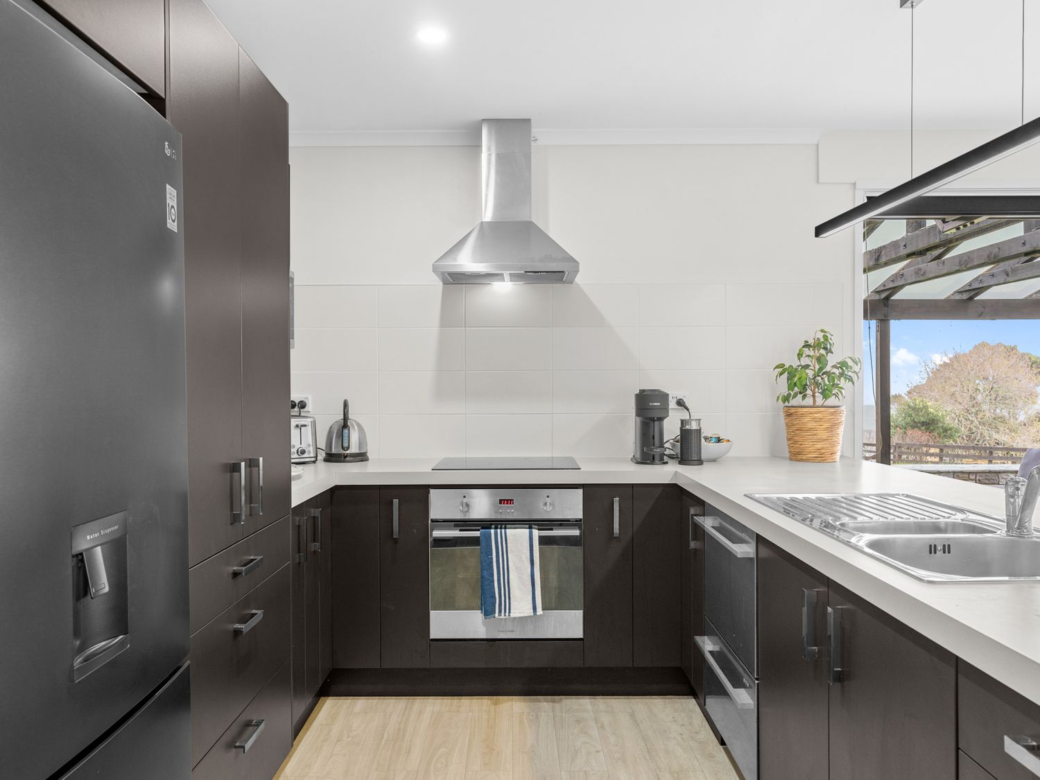A kitchen with dark cabinets a stainless steel oven and range hood a refrigerator a sink and a coffee maker at Mangawhai Maketu Mangawhai Holiday Home