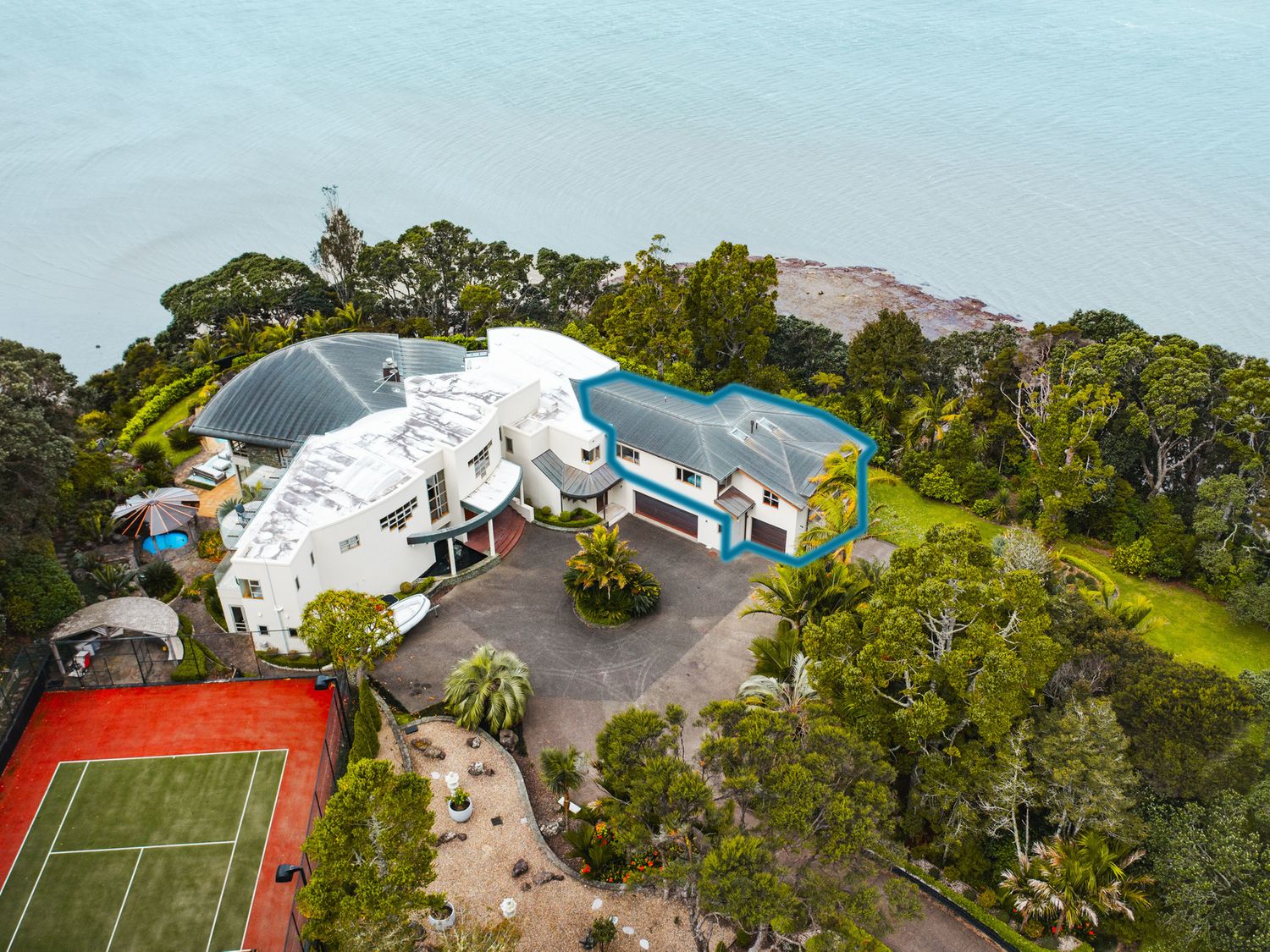 Aerial view of a property with a tennis court driveway and garden near a body of water at Beachside Luxury - Laingholm Holiday Apartment in Laingholm 24km from Auckland CBD