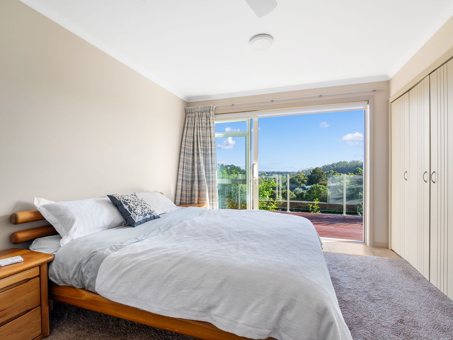 A bedroom with a wooden bed white bedding nightstand sliding glass doors leading to a balcony and built in closets at RidgeRaj - Kerikeri Holiday Home in Kerikeri