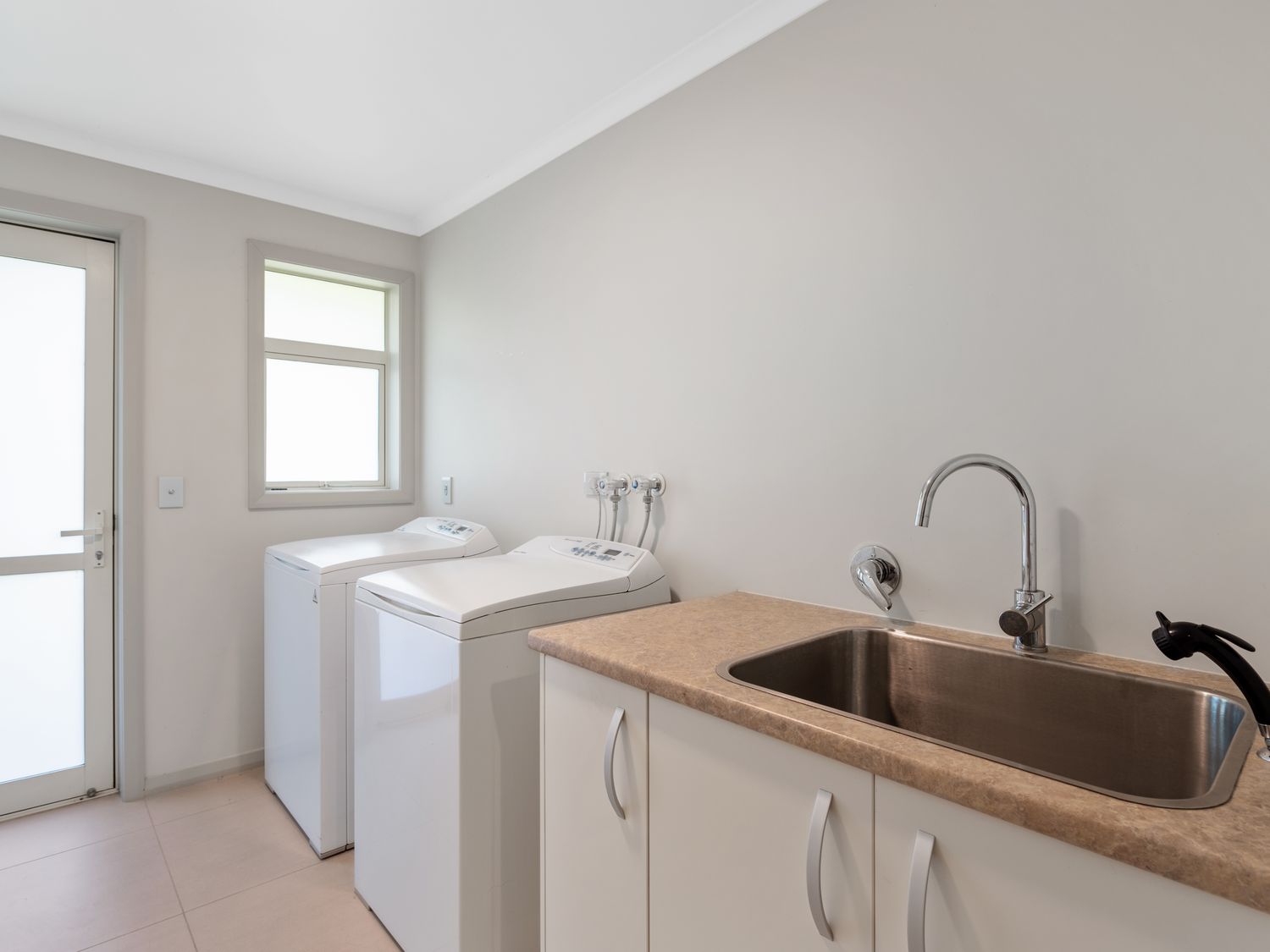 A laundry room with two washing machines a sink and storage cabinets at RidgeRaj - Kerikeri Holiday Home in Kerikeri