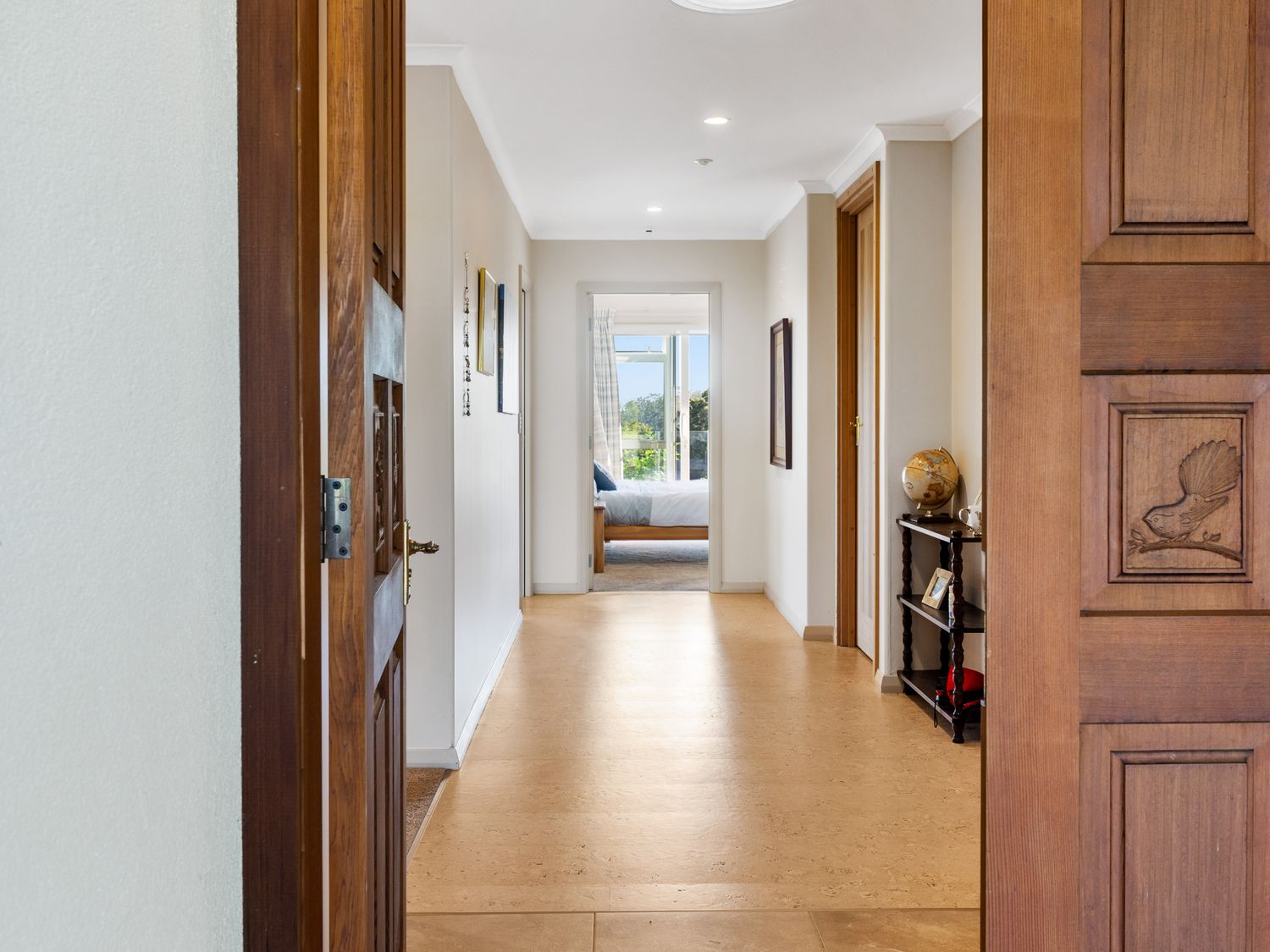 A hallway with wooden doors leading to a bedroom and a small shelf with a globe at RidgeRaj Kerikeri Holiday Home in Kerikeri