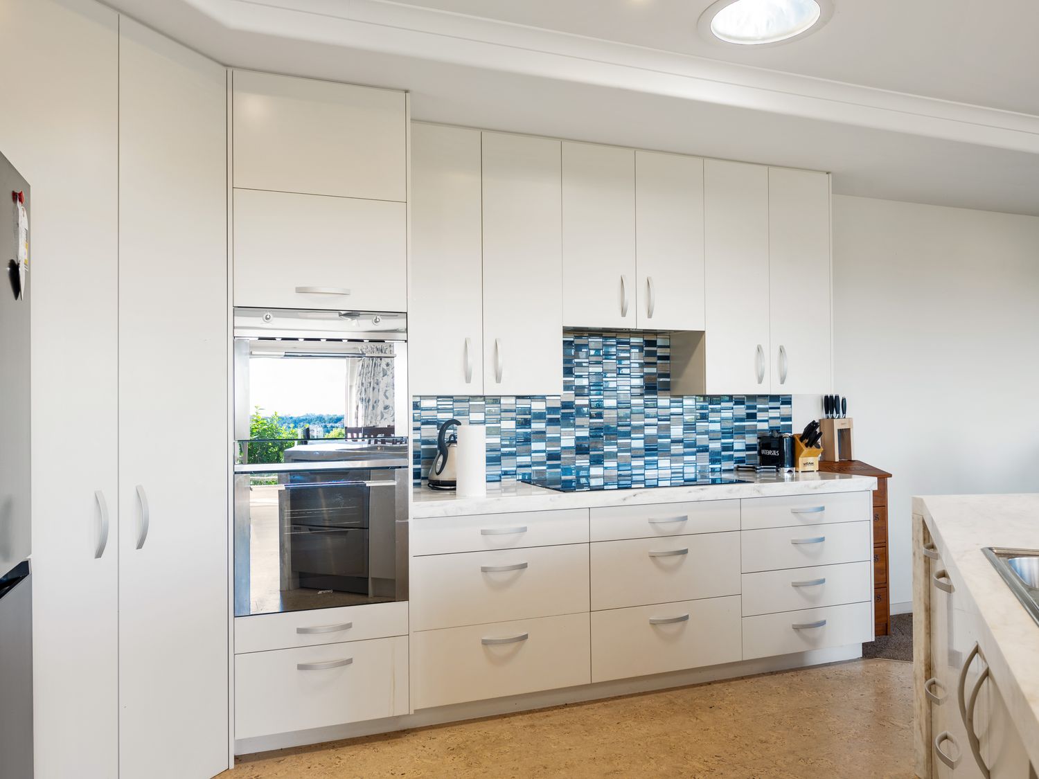 A kitchen with white cabinets a blue tiled backsplash an oven and countertop appliances at RidgeRaj - Kerikeri Holiday Home in Kerikeri