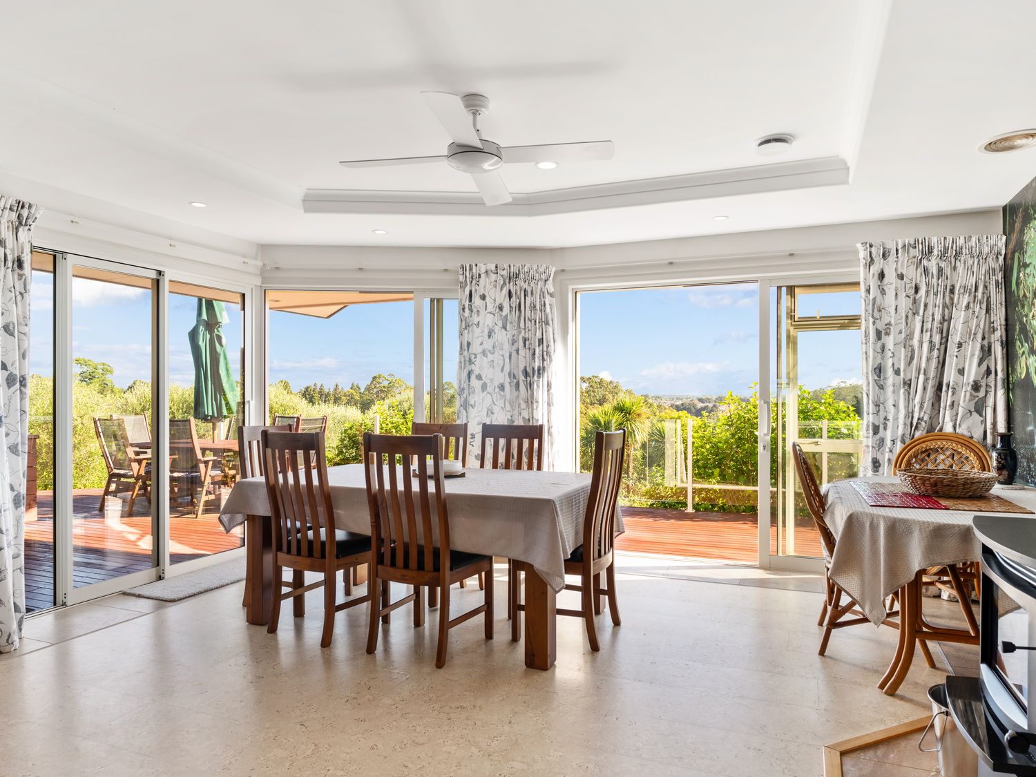 A dining room with wooden chairs and tables near large sliding glass doors at RidgeRaj - Kerikeri Holiday Home in Kerikeri