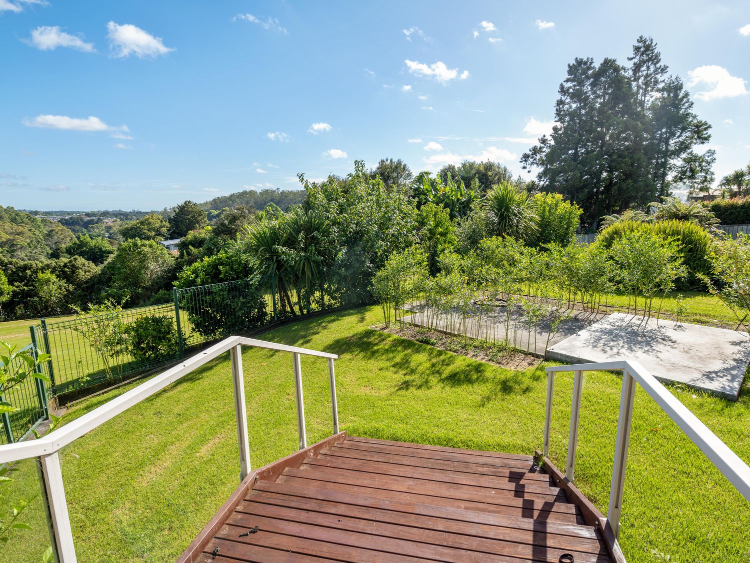 A backyard with wooden stairs leading down to a grassy area with small plants and trees at RidgeRaj - Kerikeri Holiday Home in Kerikeri