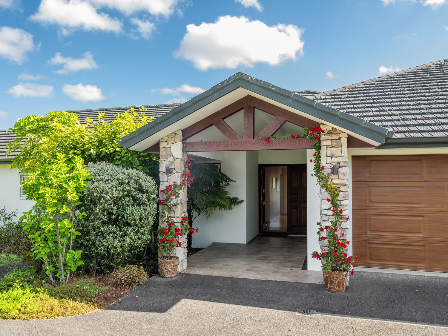 Entrance of a house with stone pillars, potted plants with red flowers, and a wooden garage door at RidgeRaj - Kerikeri Holiday Home in Kerikeri