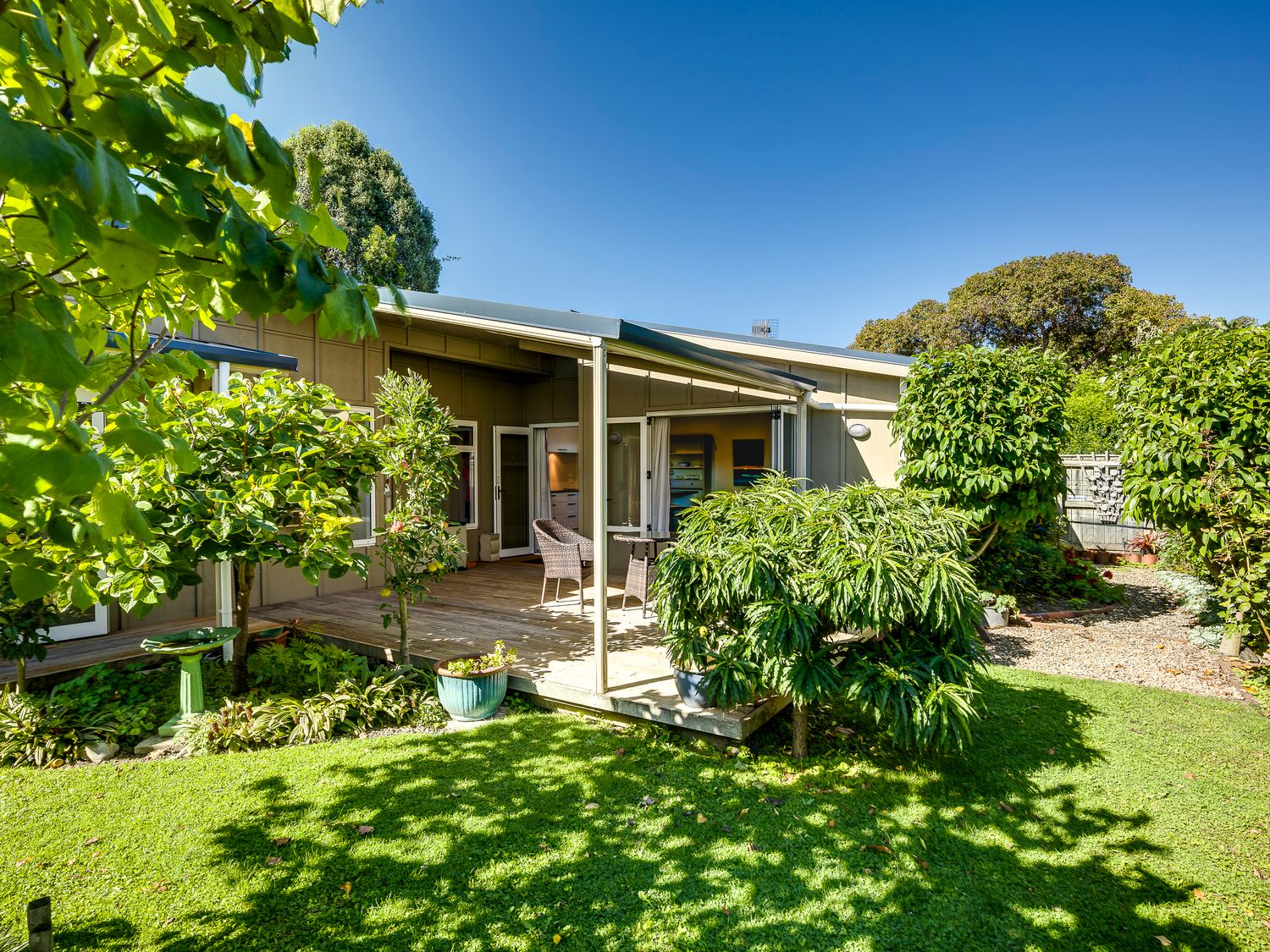 A garden with green grass trees and a wooden patio with chairs and a table at Garden Retreat in Napier