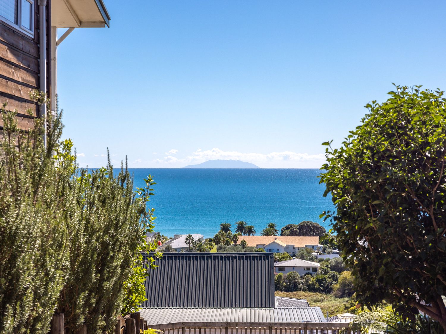 A view of the ocean with rooftops and trees in the foreground at Oceanview Magic - Onetangi Holiday Home in Onetangi