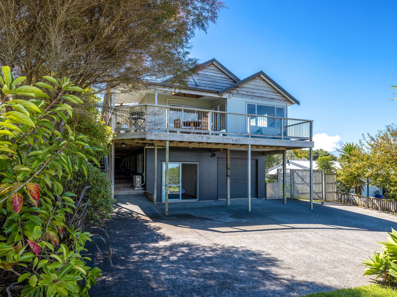 A two story house with balcony and driveway surrounded by trees and plants at Surfdale Sunspot Spa Escape Waiheke in Surfdale