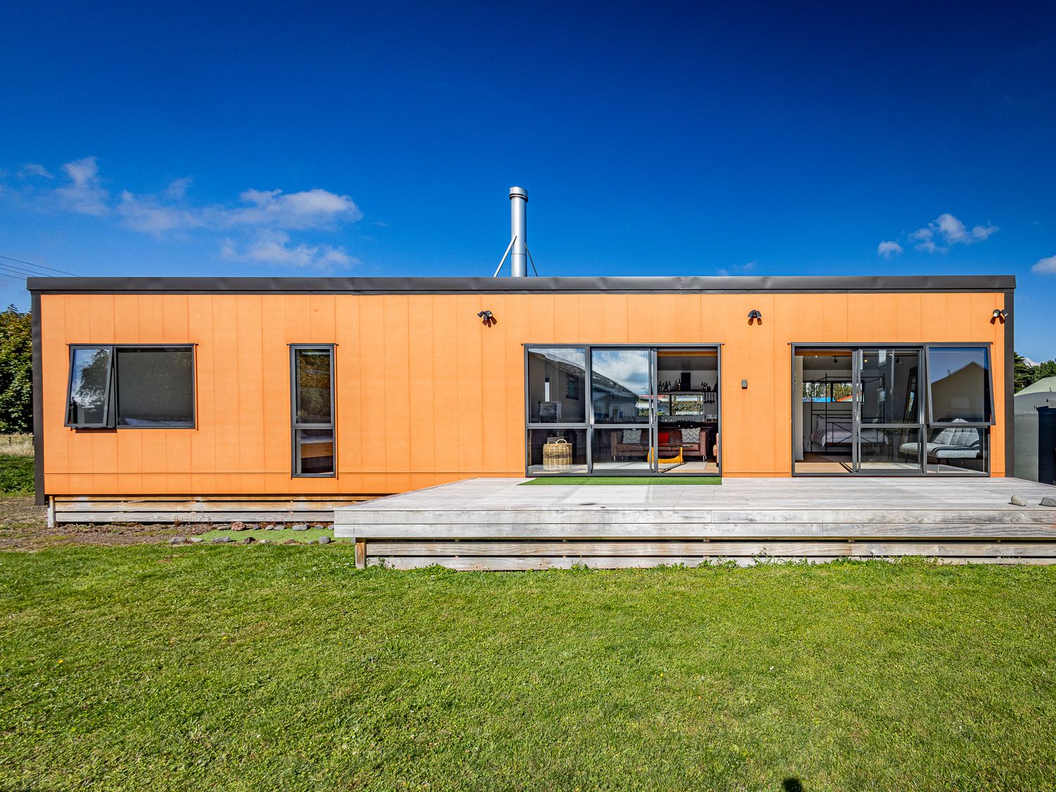 A single story rectangular house with orange walls and large windows on a grassy lawn at Te Whare Retireti Hukarere - Rangataua Retreat