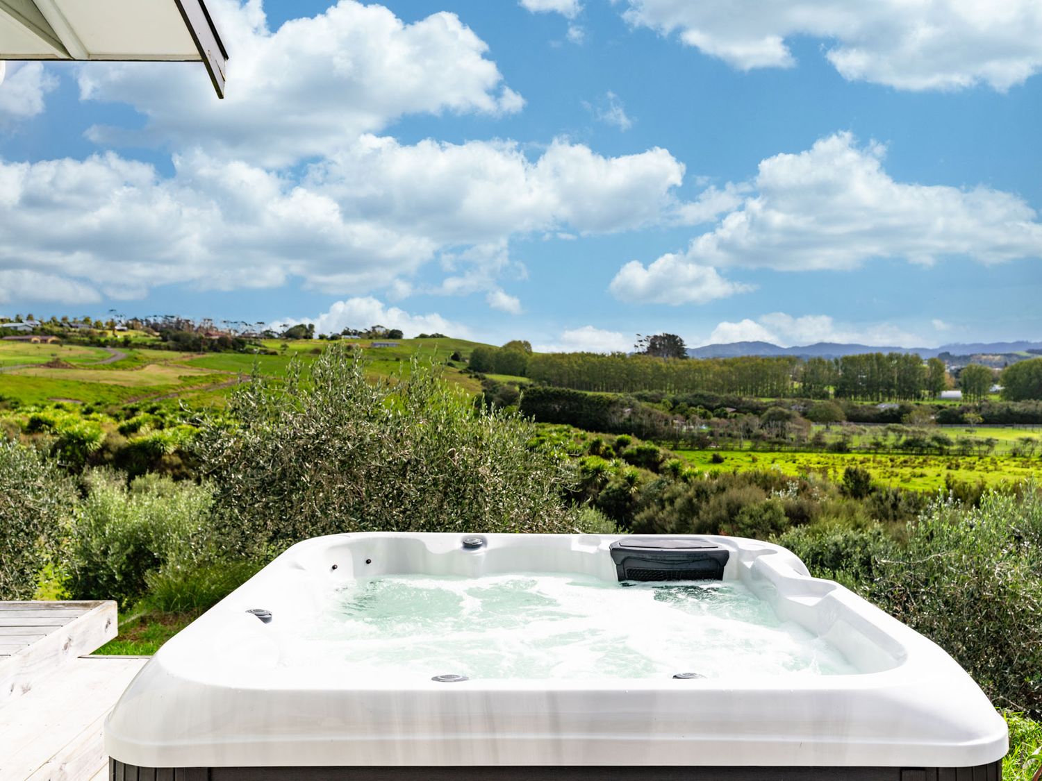 An outdoor hot tub with bubbling water overlooking green fields and hills at The Olive Hut - Mangawhai Holiday Home in Mangawhai