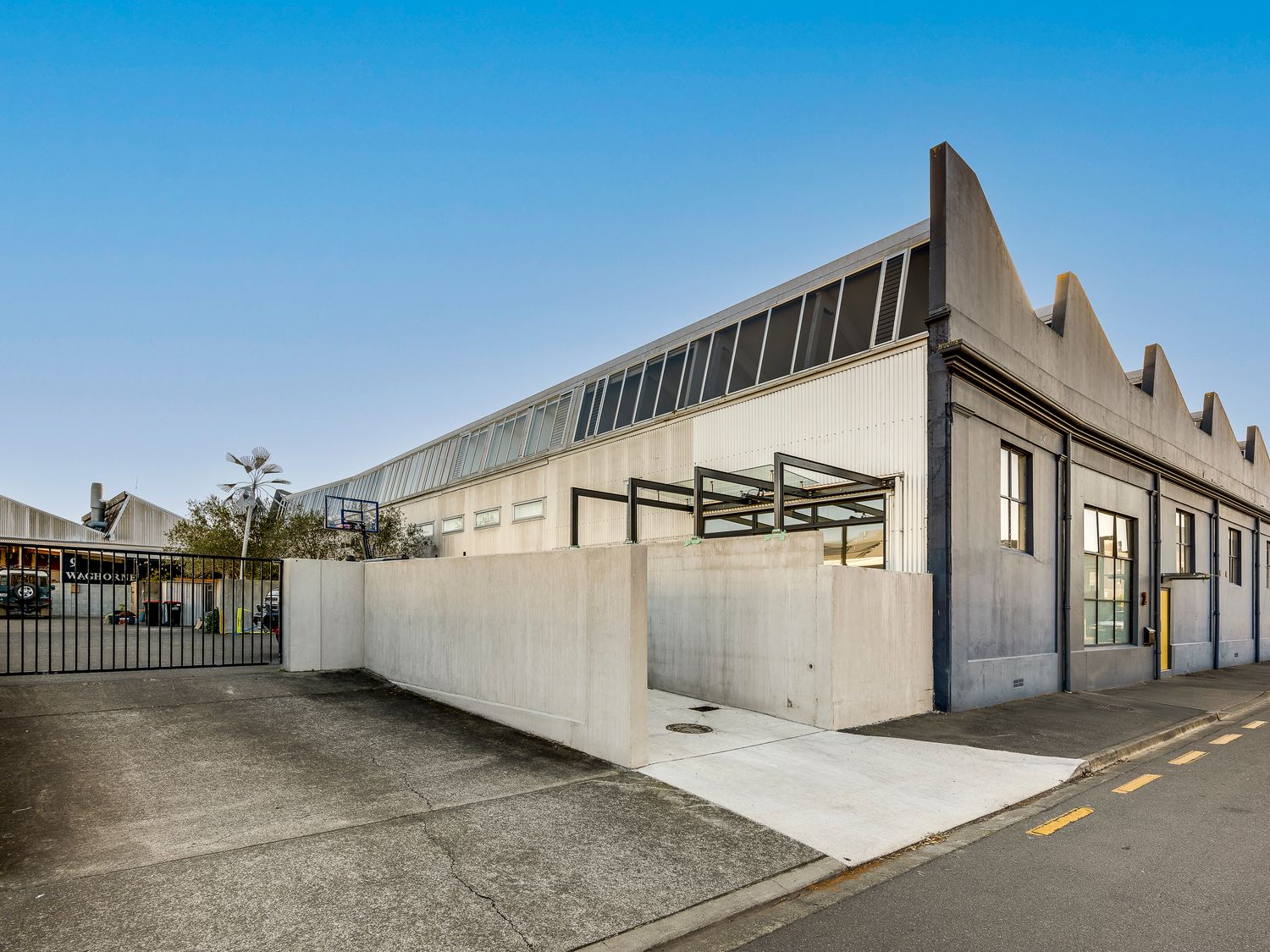 An industrial building with a tall concrete wall and a metal gate on a street at Urban Stellar - Hawkes Bay Holiday Home in Ahuriri