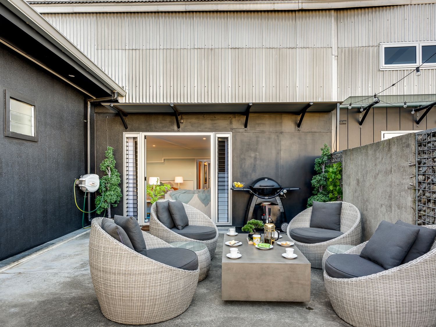 An outdoor patio with four rounded wicker chairs around a concrete table at Urban Stellar - Hawkes Bay Holiday Home in Ahuriri
