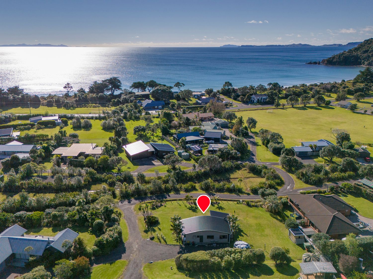 An aerial view of houses near the coast with a field and the ocean in the background at Wai Whare -  Kuaotunu Holiday Home in Kuaotunu