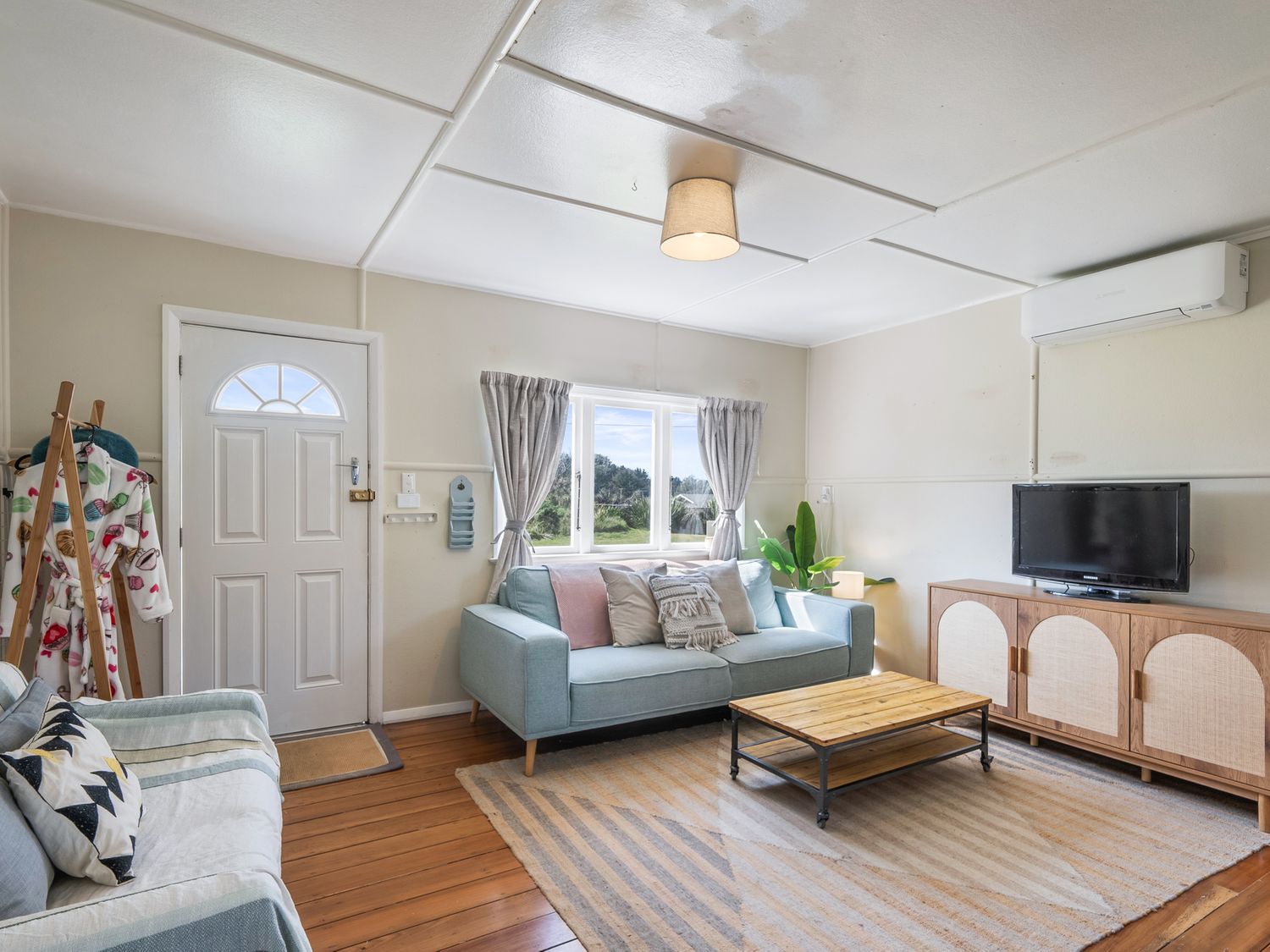 A living room with two sofas a wooden coffee table a rug a TV on a wooden cabinet and a window at Foxton Breeze - Foxton Beach Holiday Home in Foxton