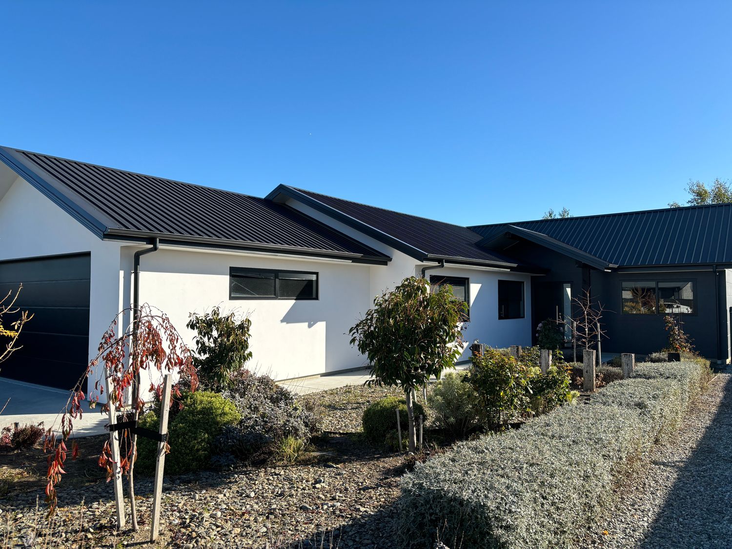 A modern single-story house with a black roof white and black walls and a landscaped garden in front at Pedal and Play - Cromwell Holiday Home in Cromwell