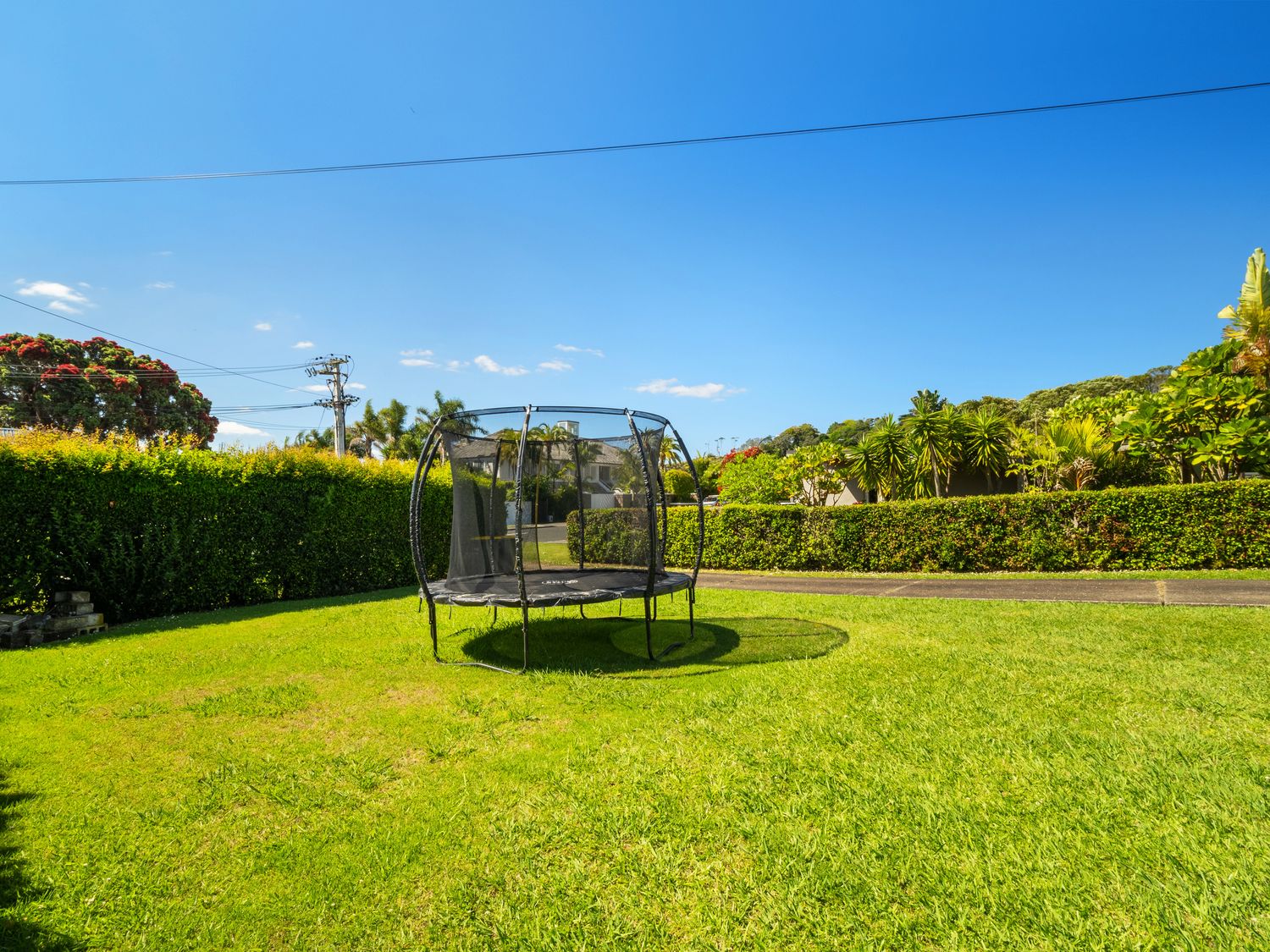 A backyard with a trampoline and hedges under a clear blue sky in Tindalls Bay
