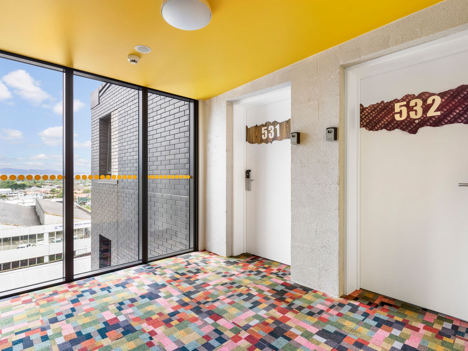 A hallway with doors numbered 531 and 532 and large windows with a city view at Layard Apartments 531 - West Auckland Apartment in Avondale