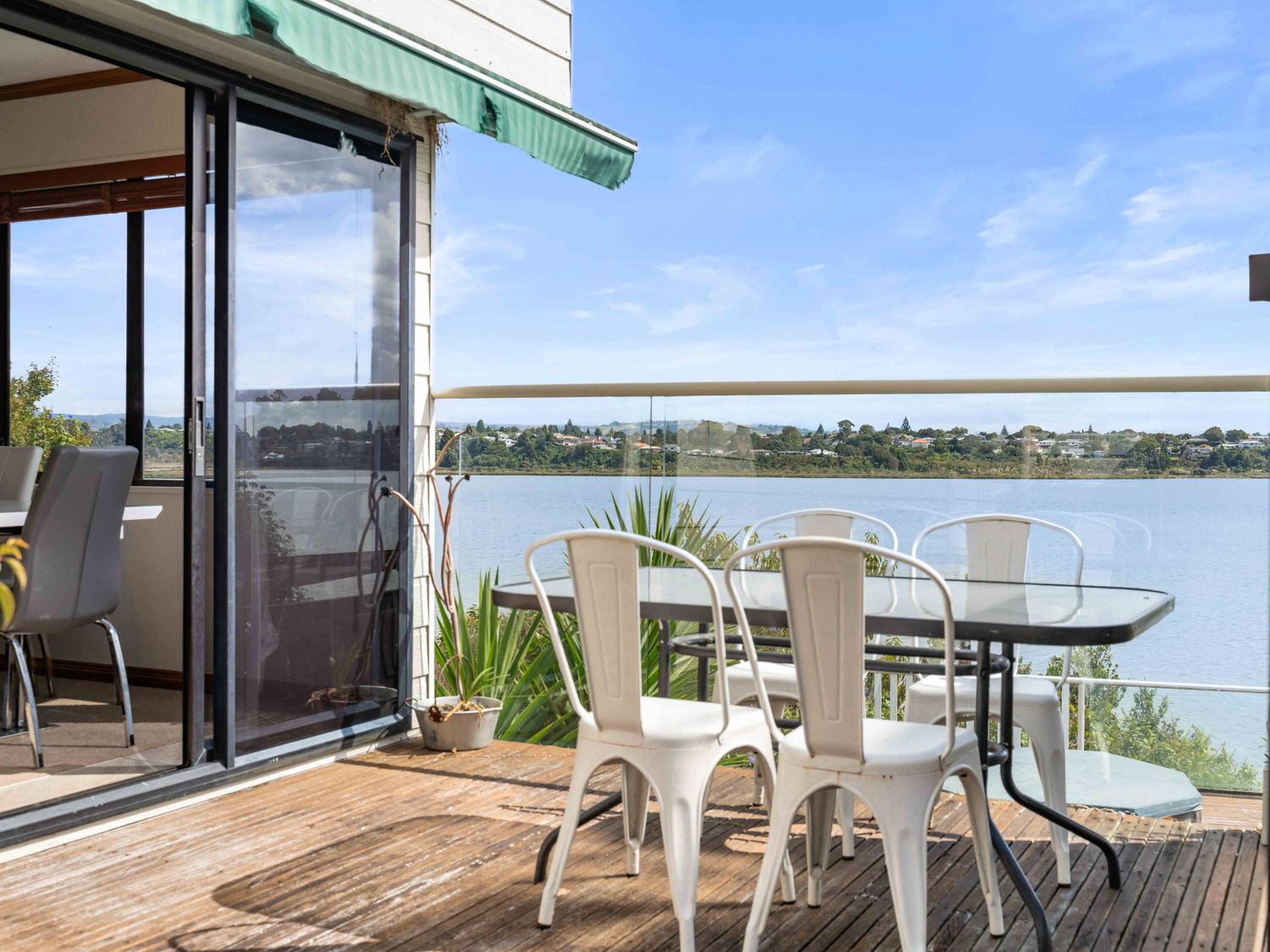 An outdoor deck with a glass table and four white metal chairs overlooking a body of water at Poolside Lookout - Tauranga Holiday Home in Hairini Tauranga