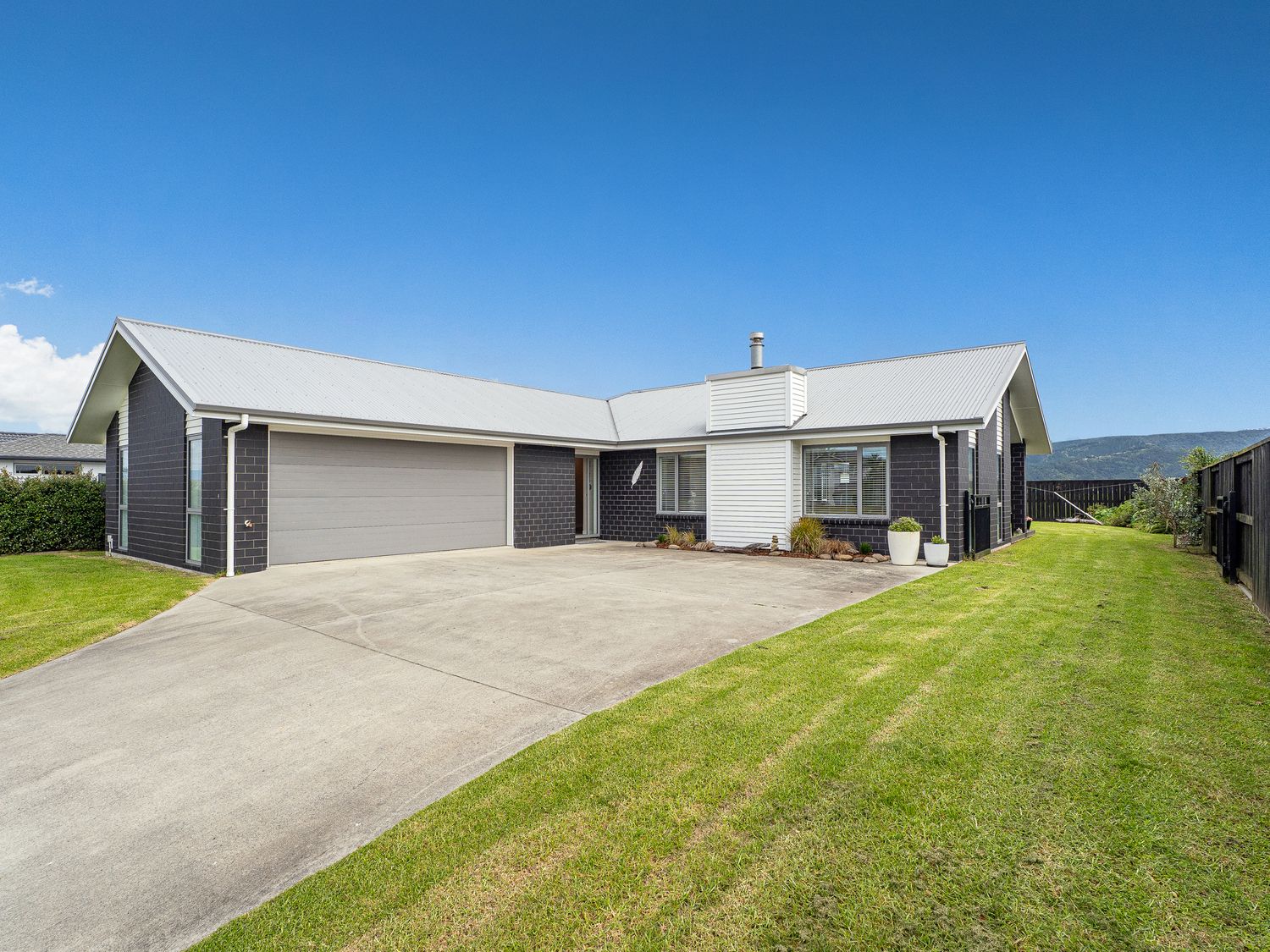 A single story house with a double garage and a concrete driveway surrounded by a lawn at Tide and Tranquility Whitianga
