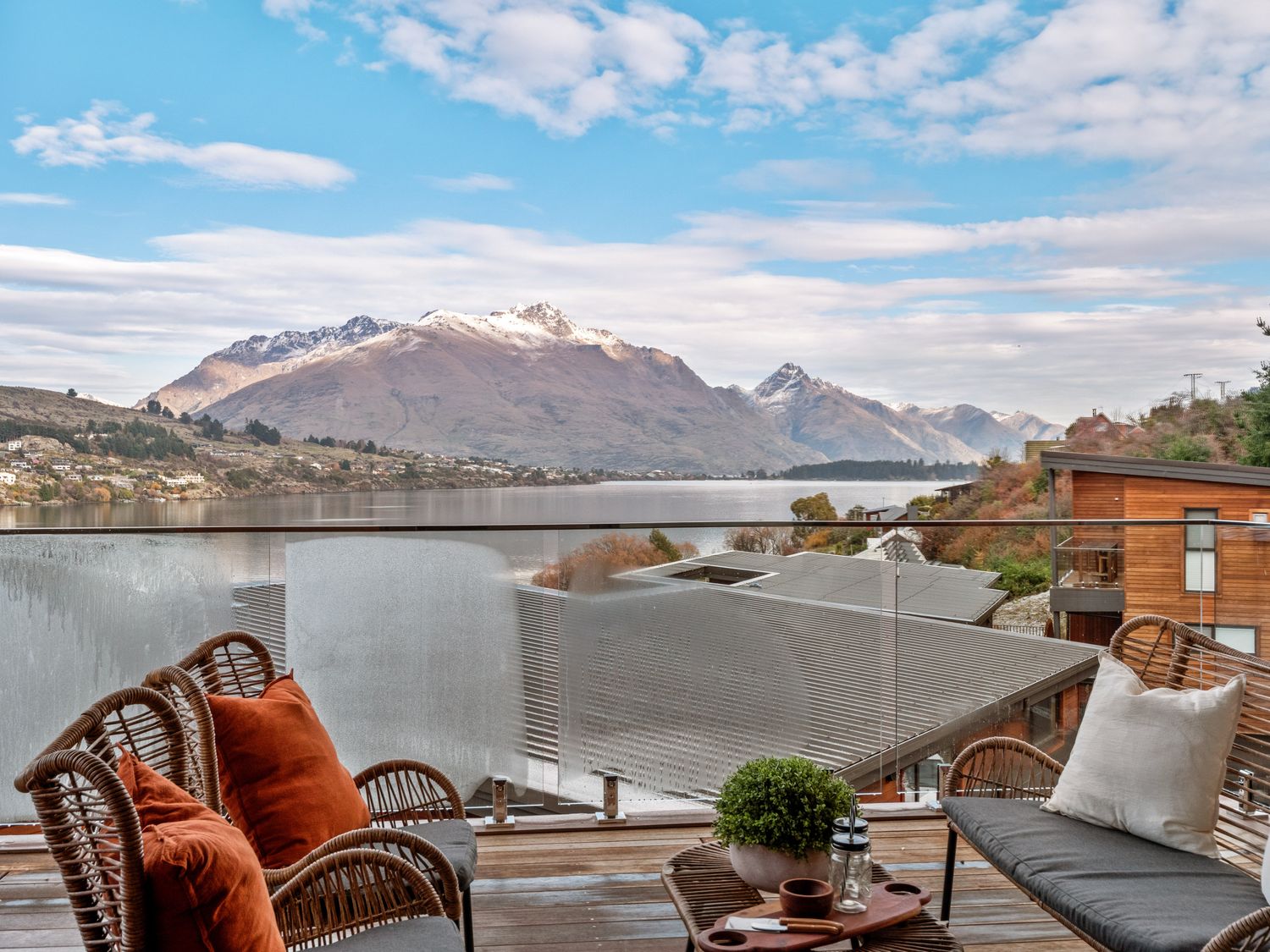 A balcony with wicker chairs and a table overlooking a lake and mountains at Remarkable QT  - Queenstown Holiday Home in Queenstown