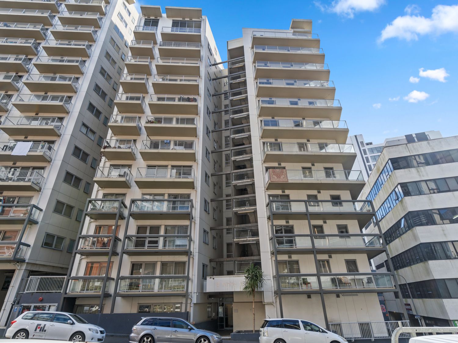 A tall residential building with multiple balconies and parked cars on the street in front of it at Cityscape on White - Auckland Central Studio in Auckland Central