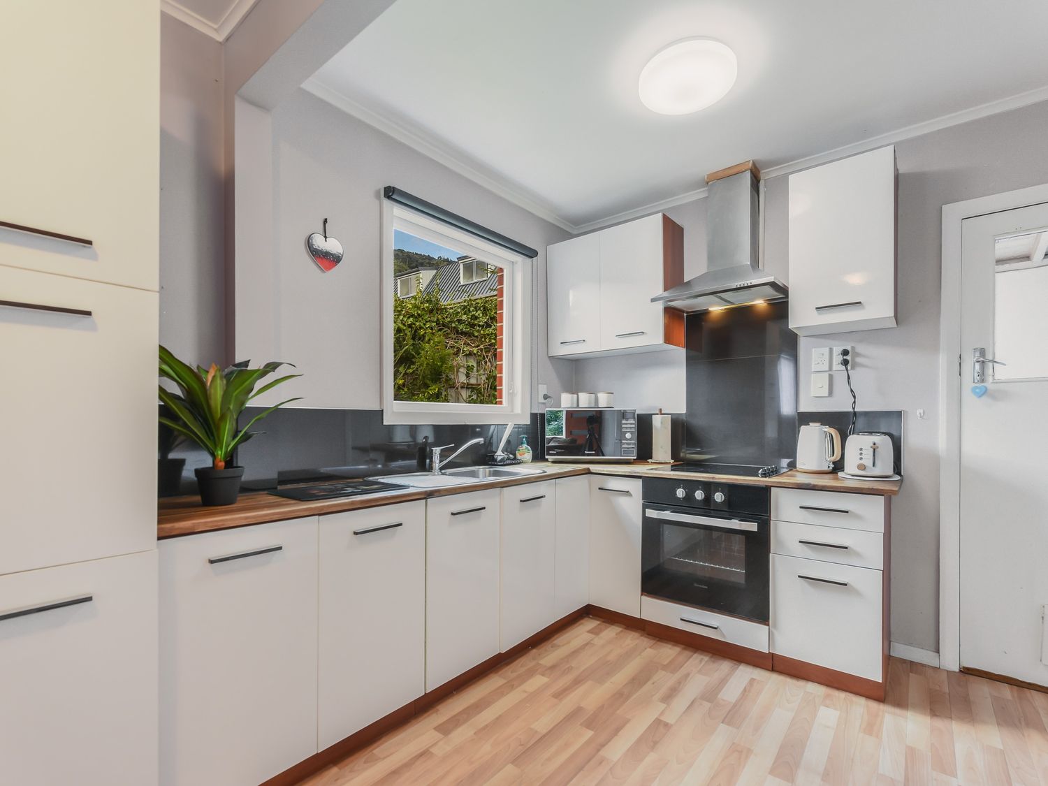A kitchen with white cabinets wooden countertops a built-in oven and a window at Picton Central Picton Holiday Home in Picton