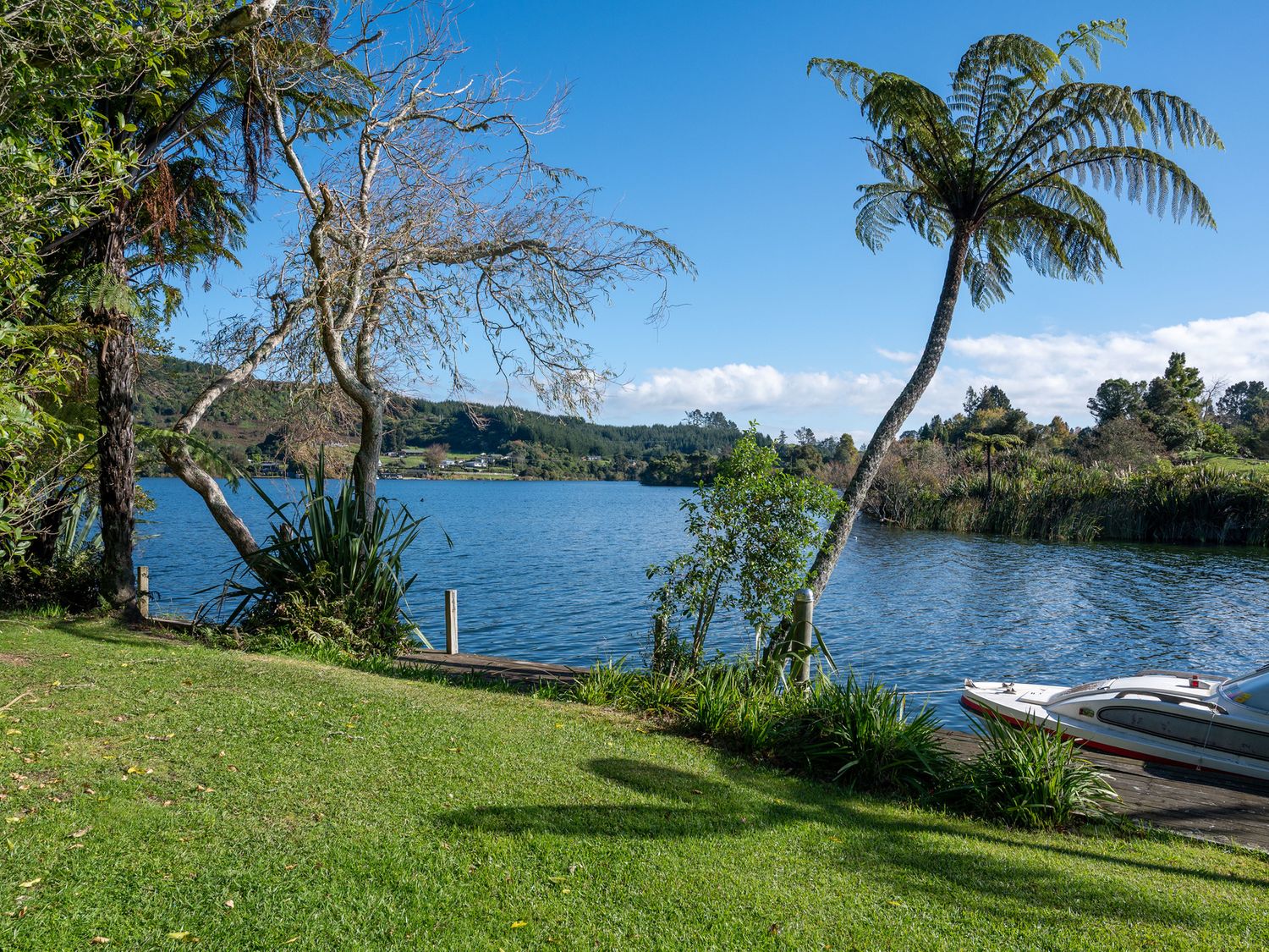 A lakeside with trees and a docked boat at Okere Jetty Escape in Okere Falls